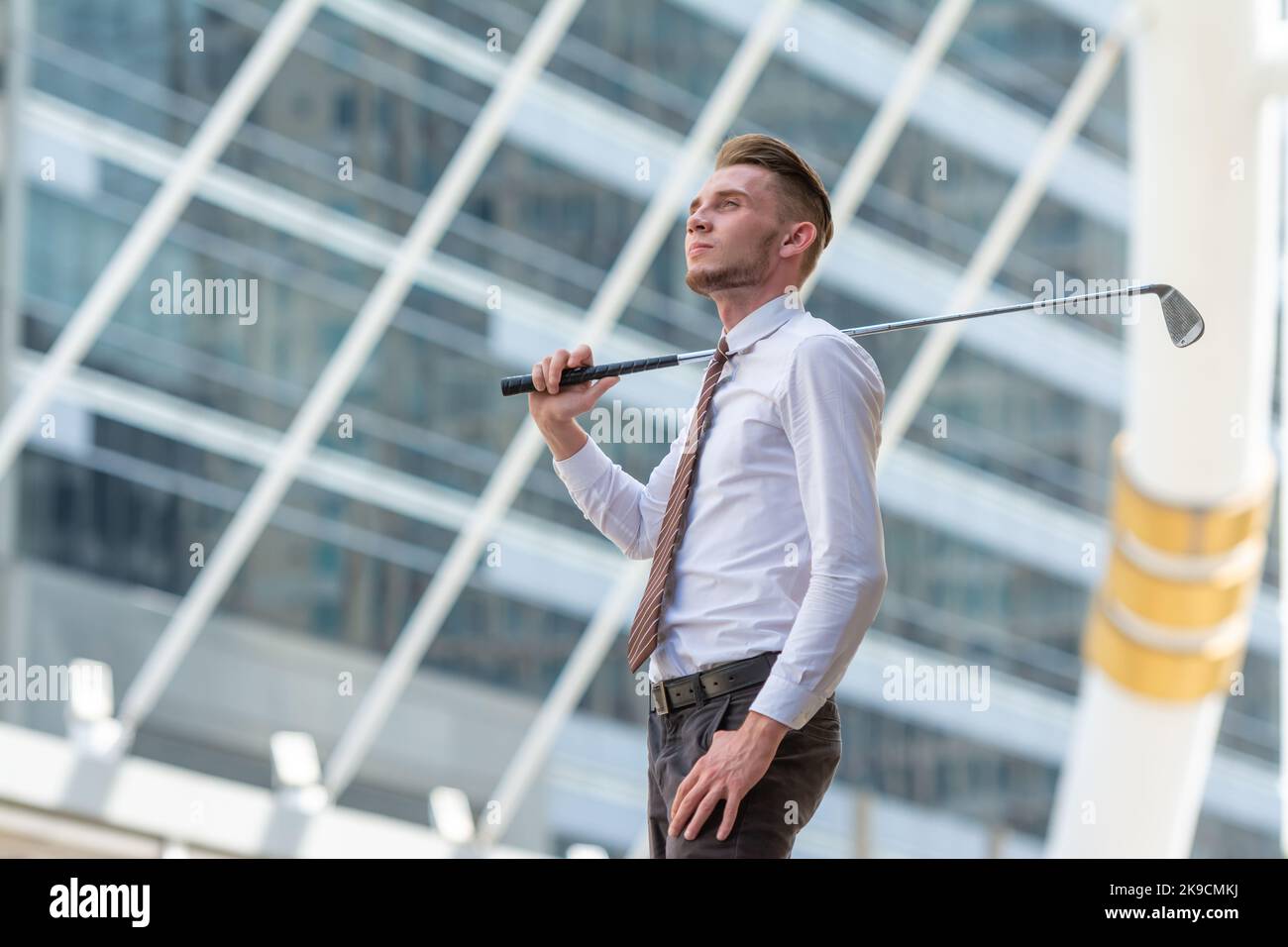 Erfolgreiche junge Küasion zuversichtlich CEO Geschäftsmann trägt weißes Hemd mit Golfclub in der Stadt Blick in den Himmel mit verträumt. Stockfoto