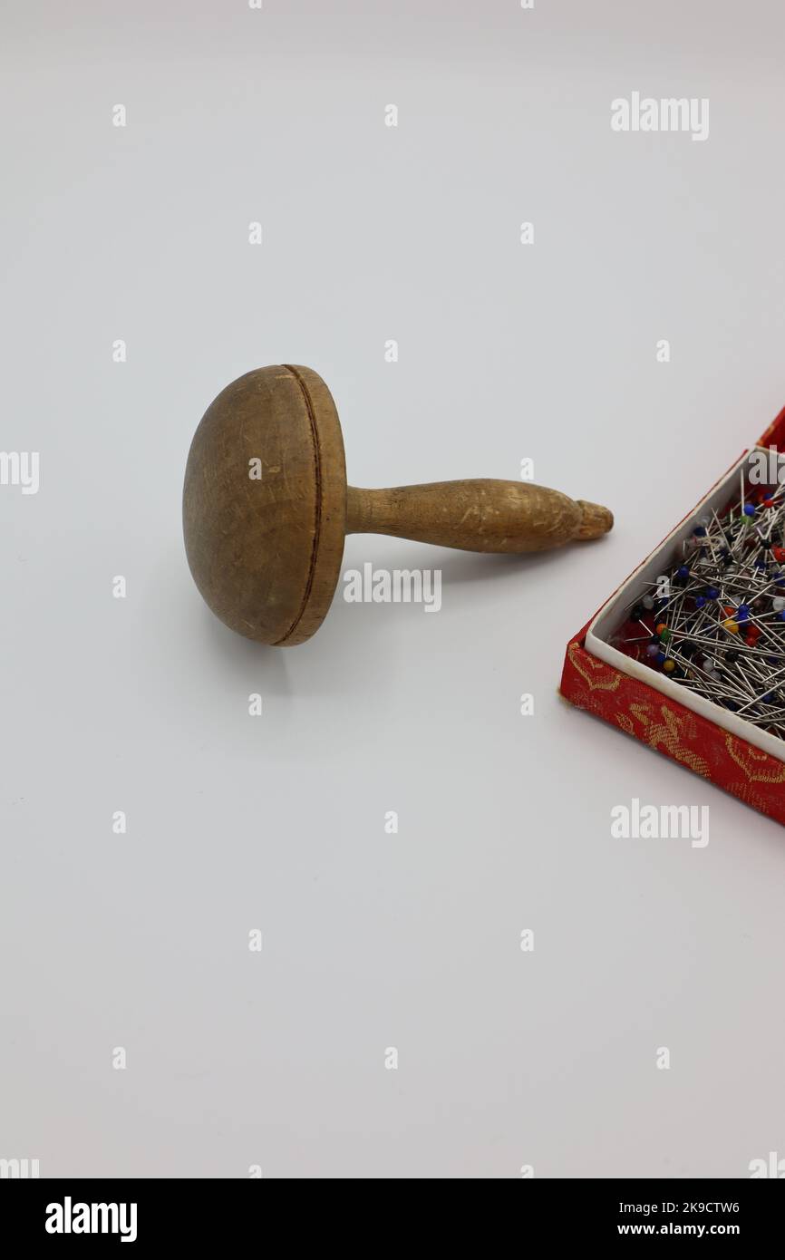 Nähen von Accessoires auf weißem Hintergrund. Stifte in einer Schachtel und ein Holzpilz, mit dem Löcher auf Kleidung, Strumpf oder Socken befestigt werden Stockfoto