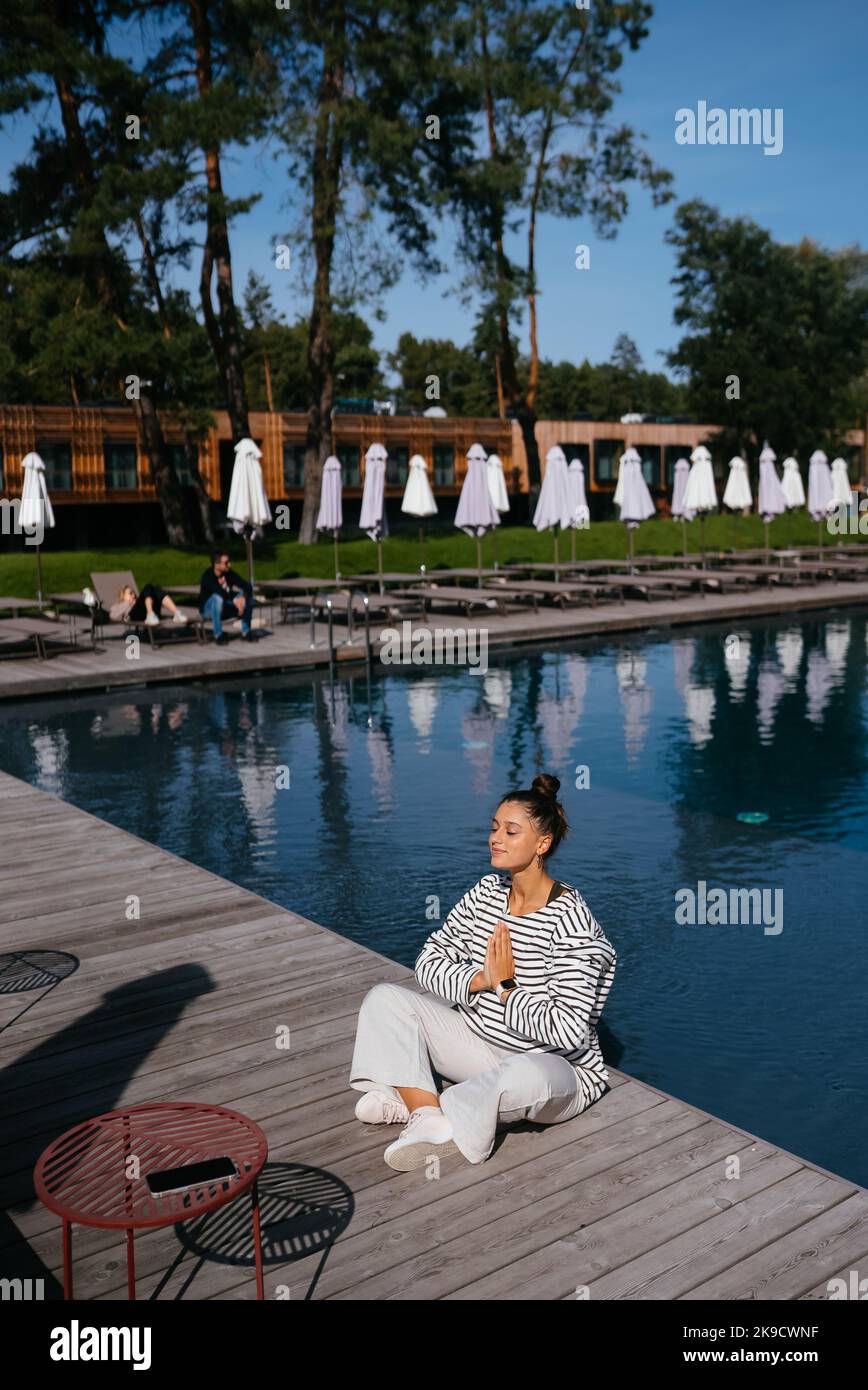 Junge Fitness-Frau, die ihren morgendlichen Yoga in der Nähe des Pools macht Stockfoto