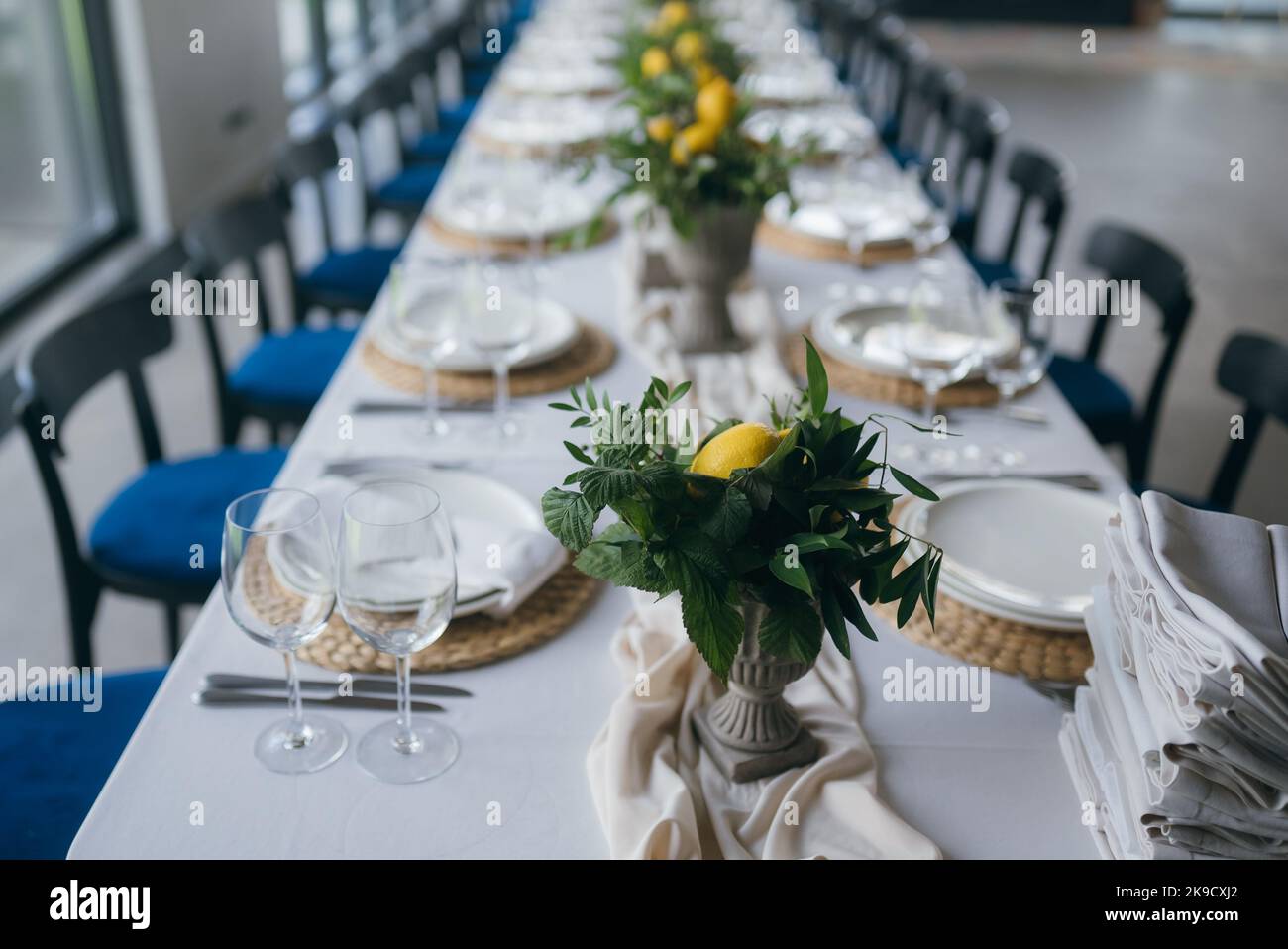 Festliche Tische auf der Hochzeitsfeier sind mit Zitronenarrangements dekoriert, auf dem Tisch sind Teller mit Servietten und Gläsern Stockfoto