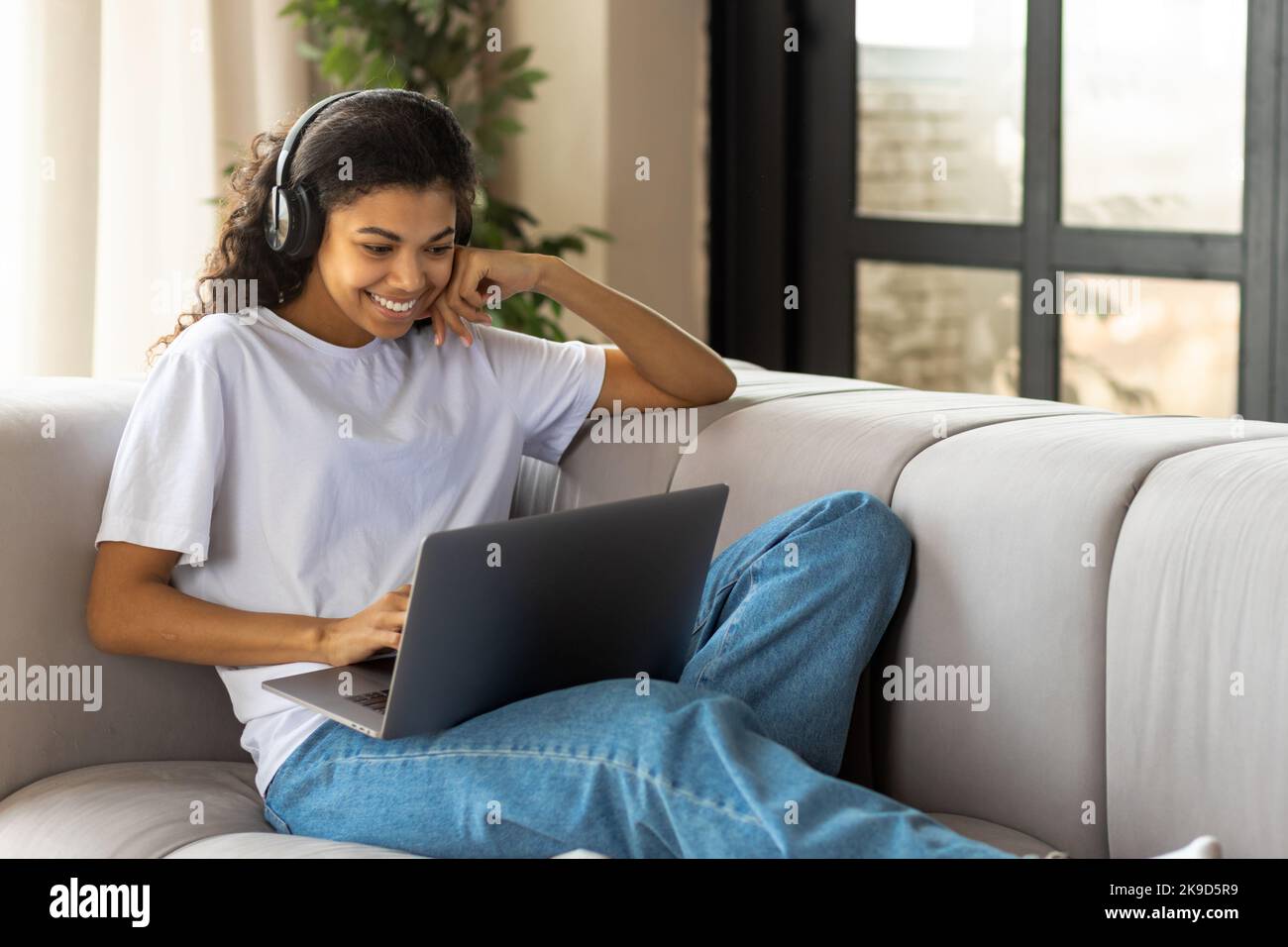 Afroamerikanische Frau im Kopfhörer mit Afro-Haaren, die einen Laptop benutzt und mit einer Freundin online mit einer Webcam spricht Stockfoto