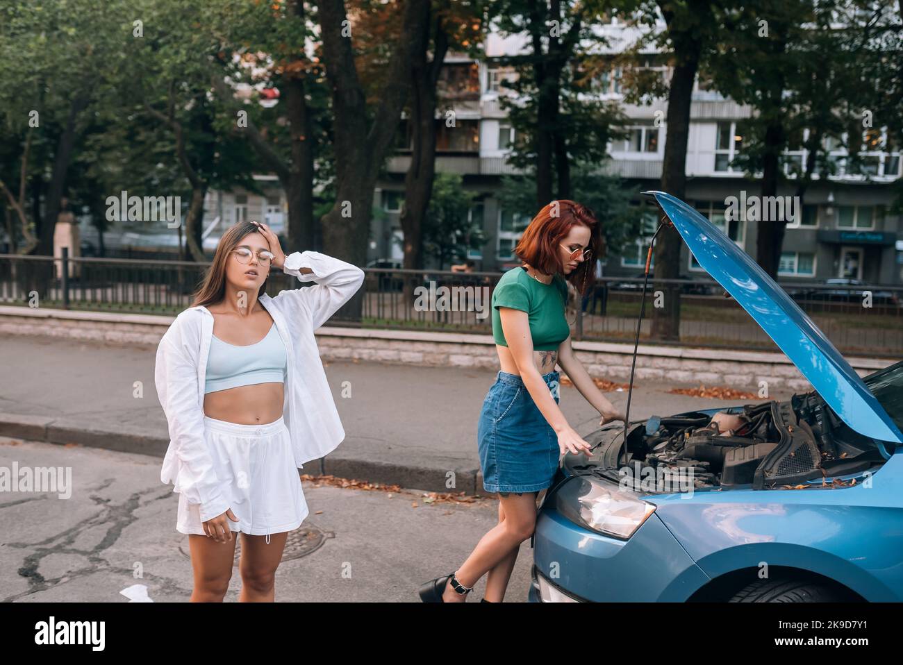 Zwei Frauen mit einem kaputten Auto auf der Straße. Haube öffnen Stockfoto