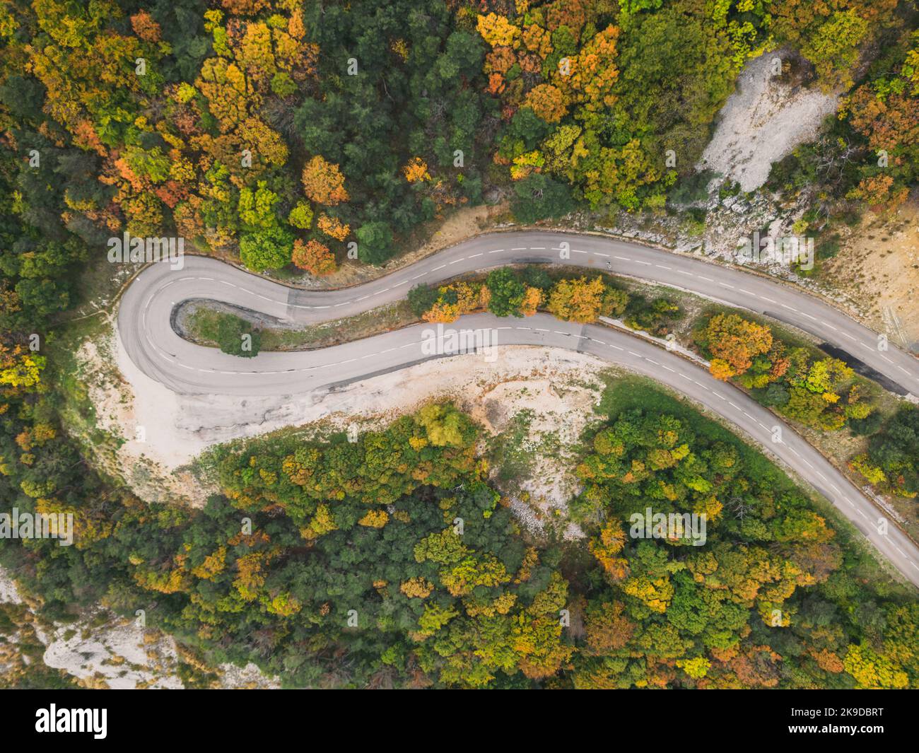 Luftaufnahme einer kurvenreichen Straße von einem hohen Bergpass durch einen dichten bunten Herbstwald. Stockfoto