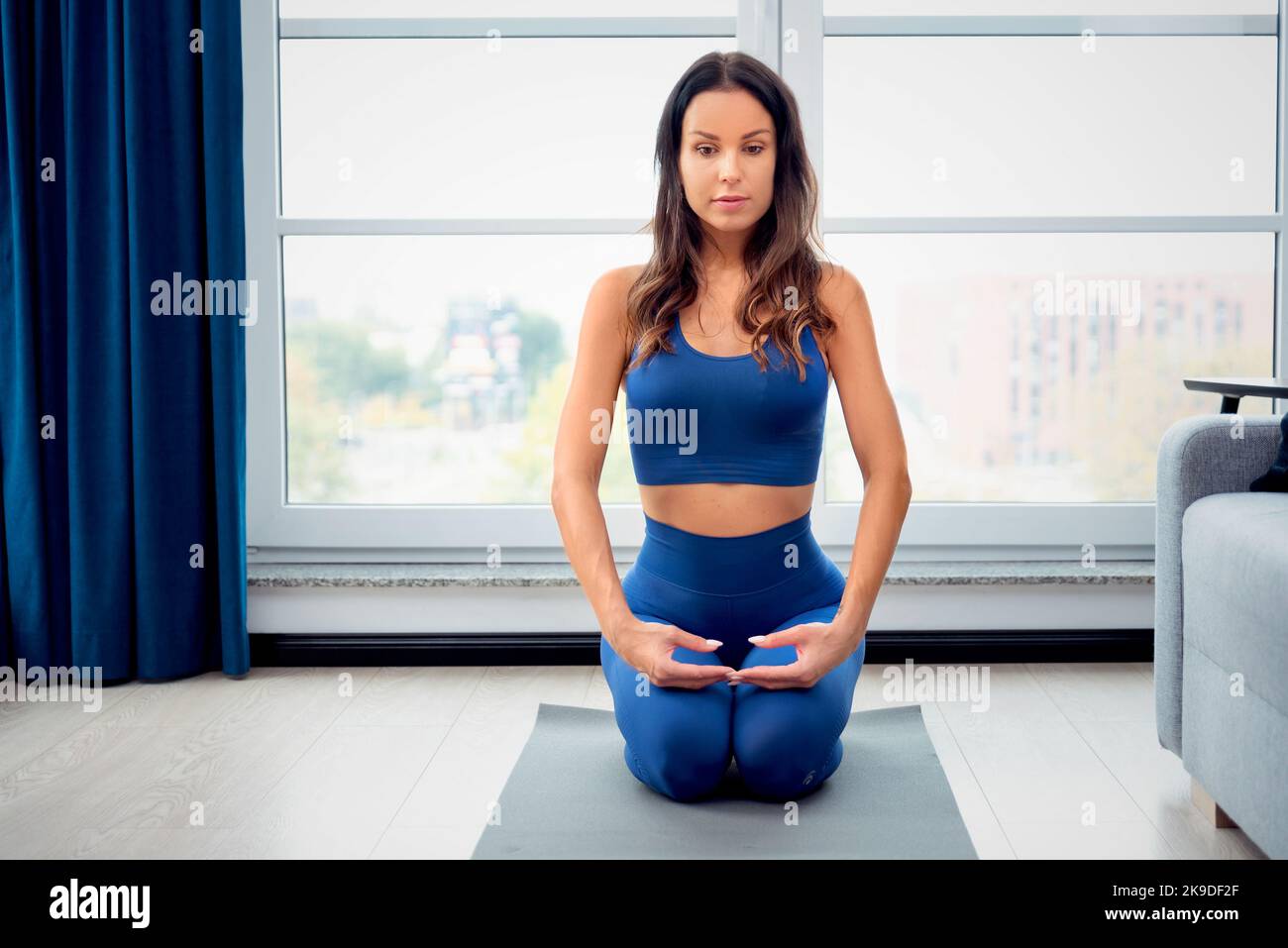 Junge Frau sitzt in Yoga-Position und meditiert zu Hause Stockfoto