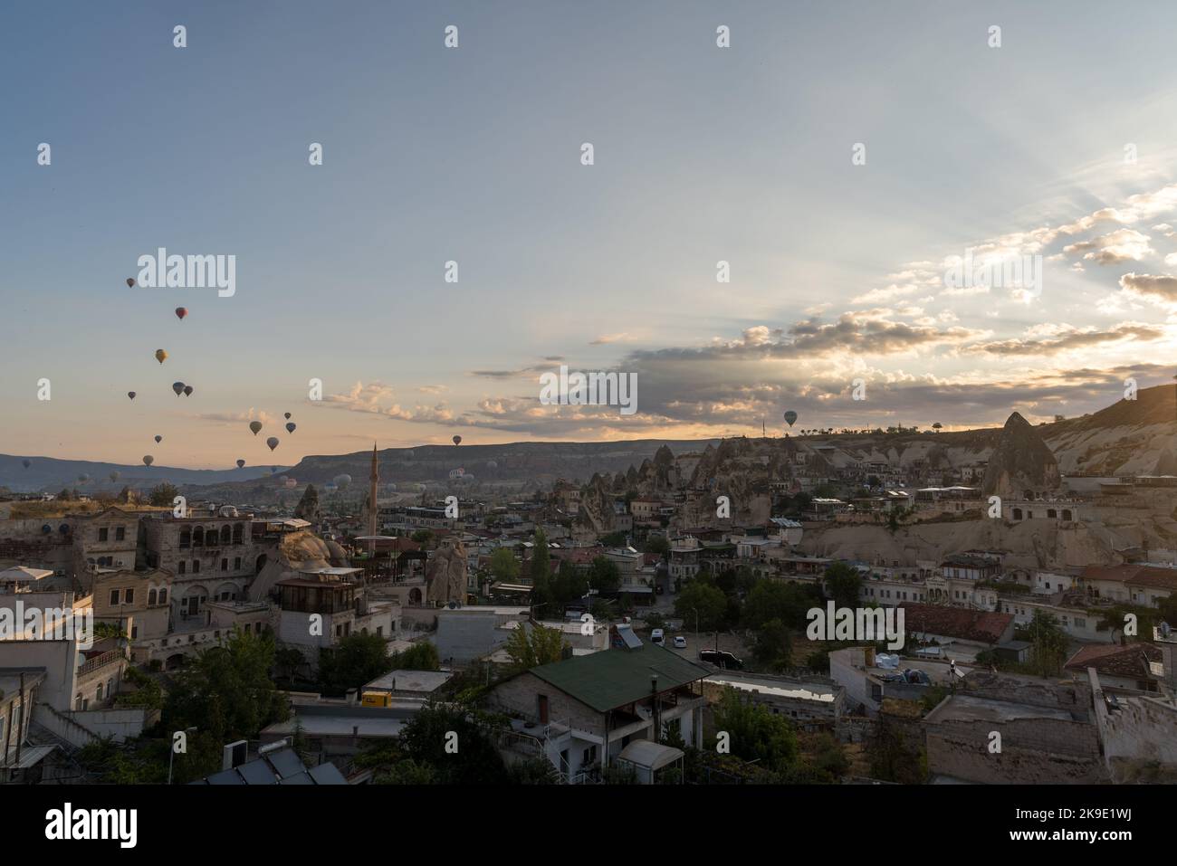 Heißluftballons fliegen über die einzigartigen Felsformationen und die Stadt Göreme bei Sonnenaufgang, Kappadokien, Türkei. Stockfoto