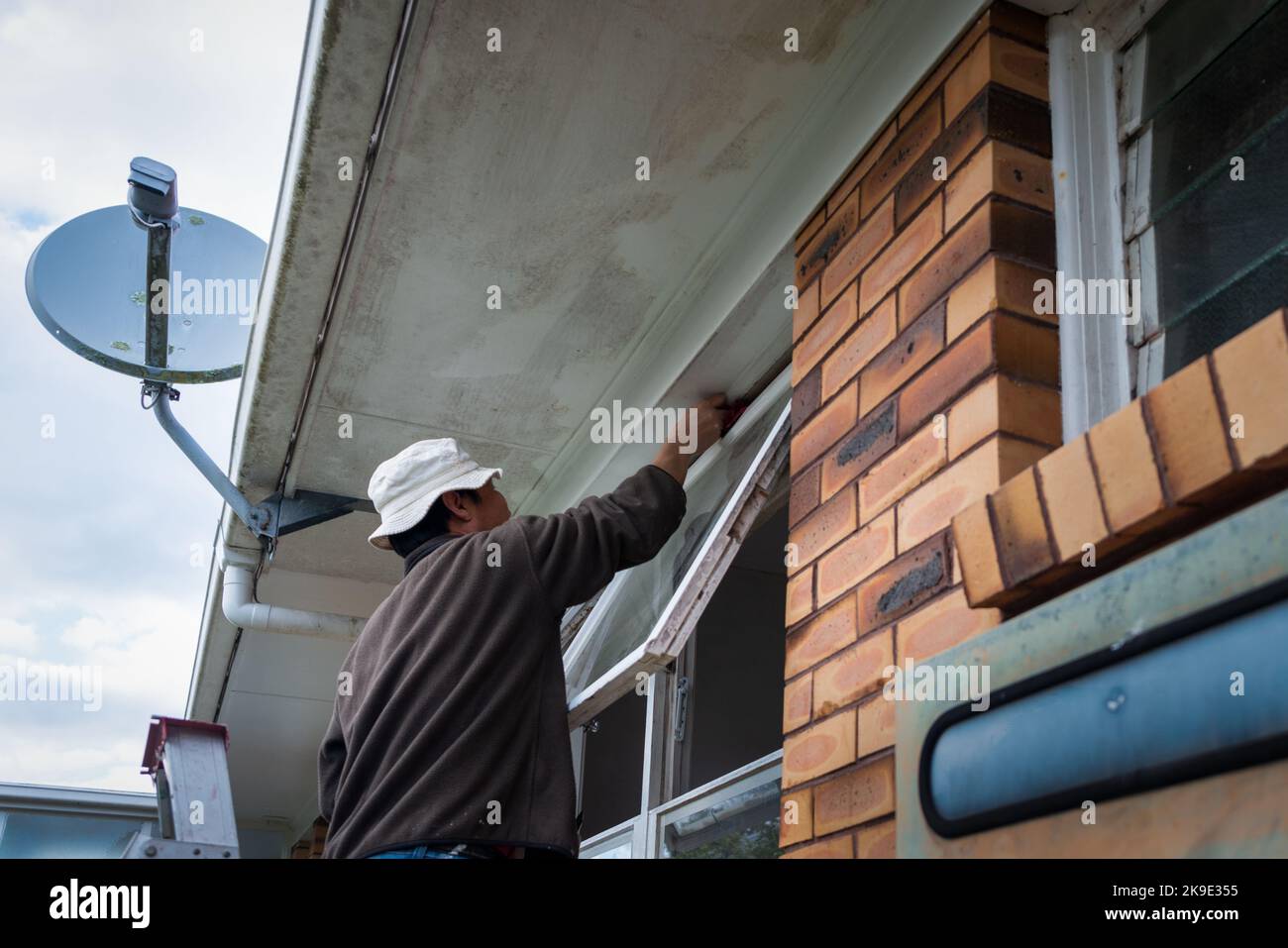 Mann, der verschimmelte Fensterrahmen eines alten Hauses putzt. Heimwartungsprojekt. Stockfoto