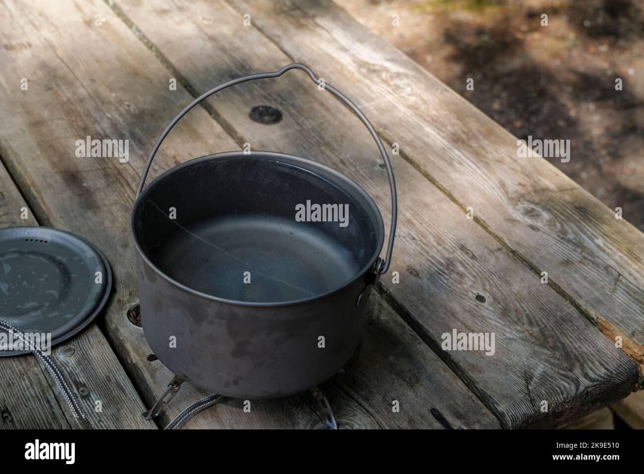 Ein Titantopf zur Herstellung von Lebensmitteln auf einem Gasherd auf einem Campingtisch aus Holz im Wald. Stockfoto