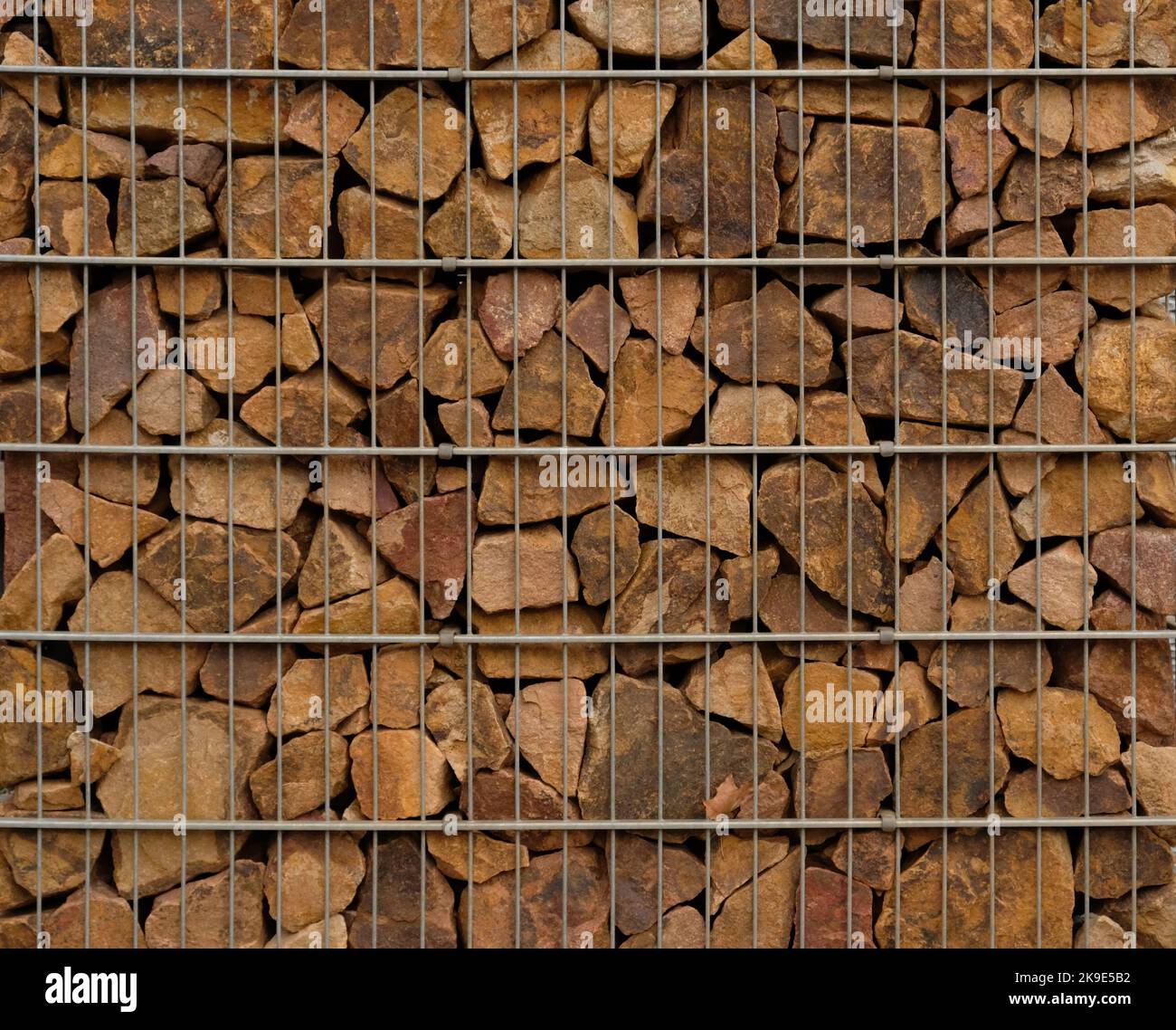 Gabion-Stützmauer - Nahaufnahme von braunen Steinen in Gabion-Metallkörben, die von einer Stützwand gehalten werden. Stockfoto