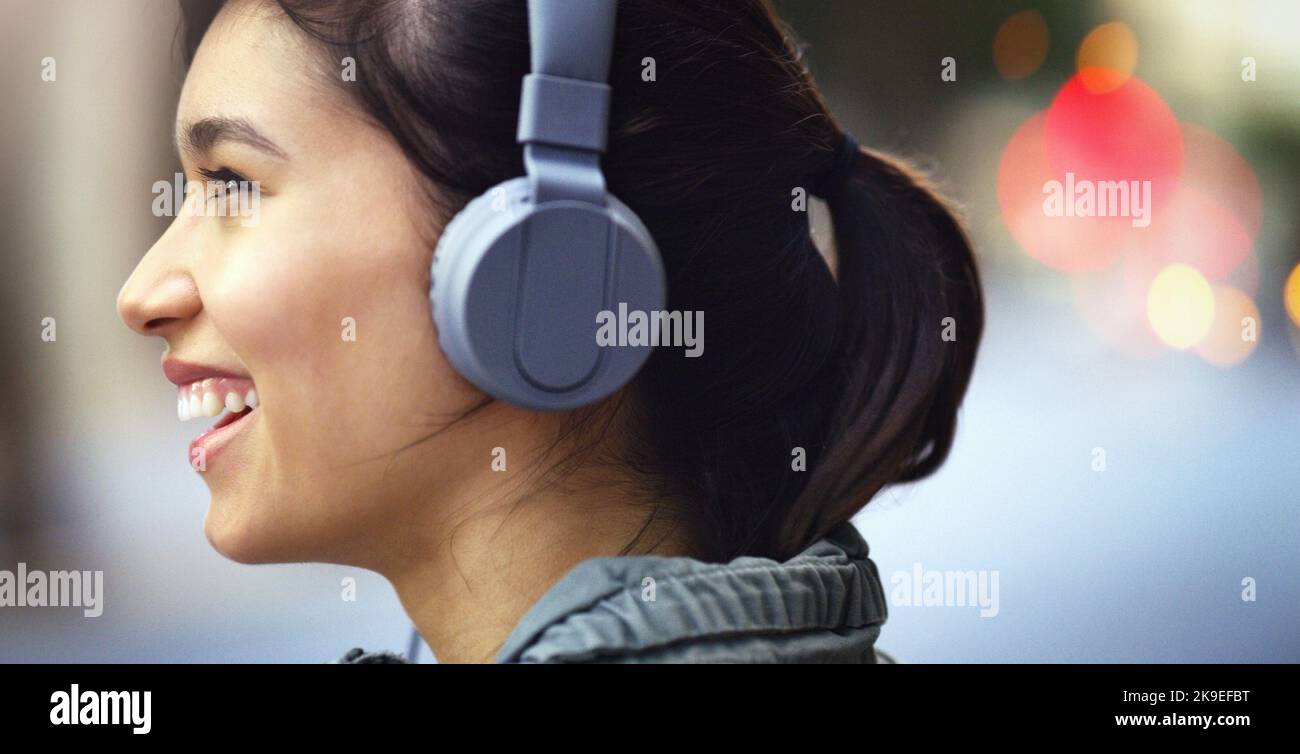 Den Lärm der Stadt zu blockieren. Nahaufnahme einer fröhlichen jungen Frau, die auf ihren Kopfhörern Musik hört, während sie durch die Stadt läuft. Stockfoto