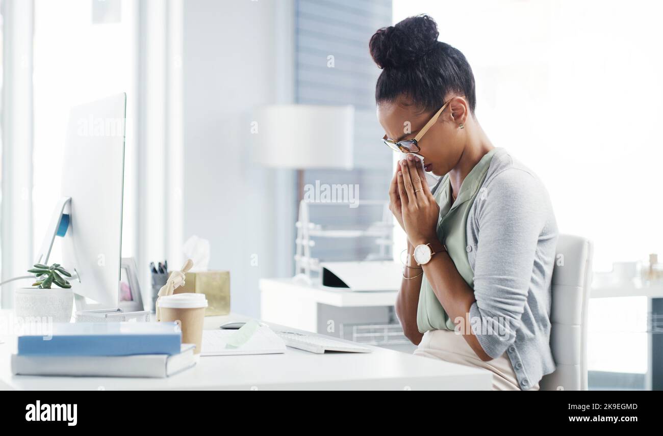 Ich glaube nicht, dass es den Rest des Tages schlecht machen kann. Eine attraktive junge Geschäftsfrau, die ihre Nase mit einem Tuch bläst, während sie an ihrem Schreibtisch in einem modernen Büro ist. Stockfoto