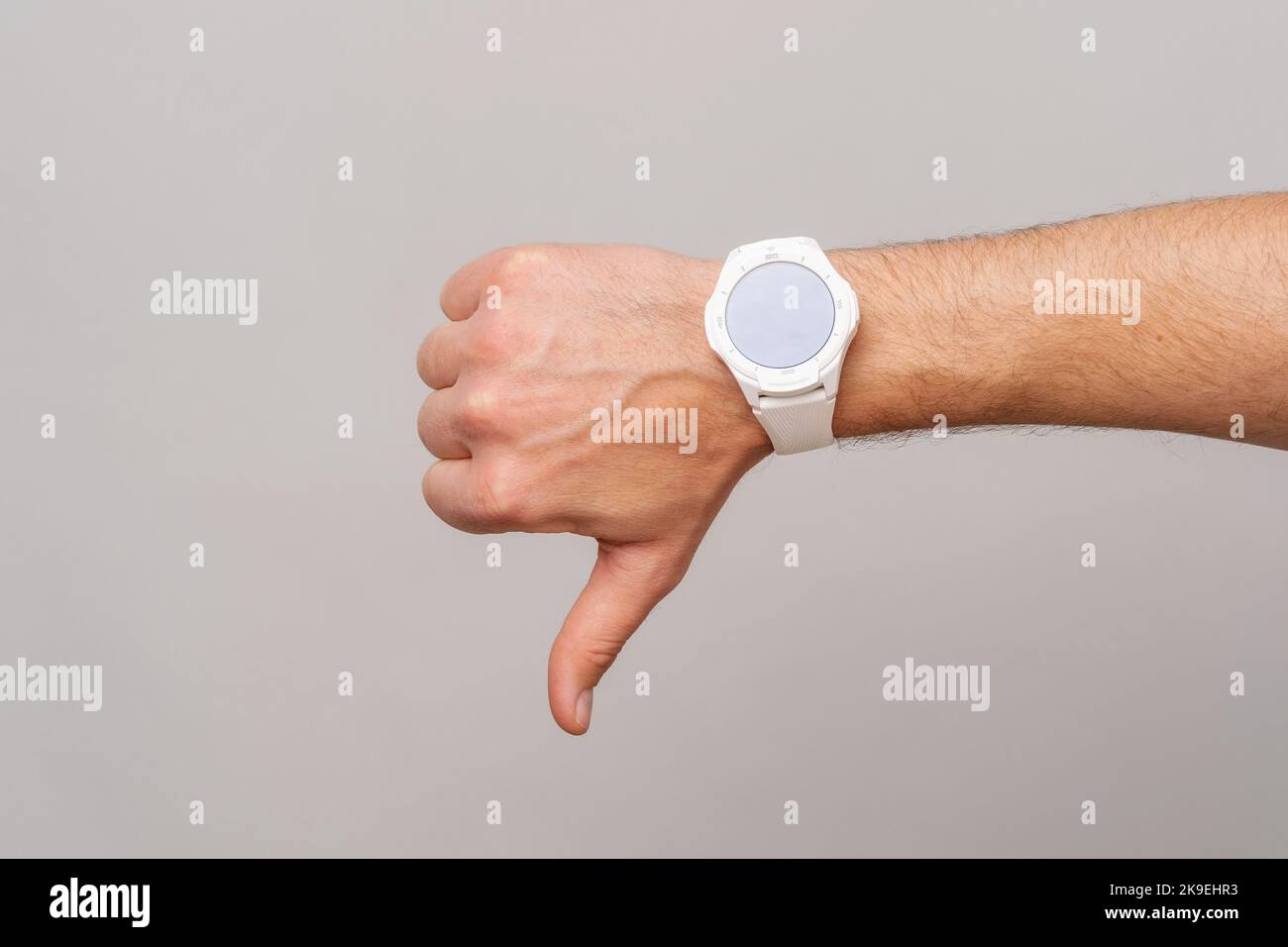 Foto einer männlichen Hand mit Smartwatch, die den Daumen auf grauem Hintergrund zeigt. Stockfoto