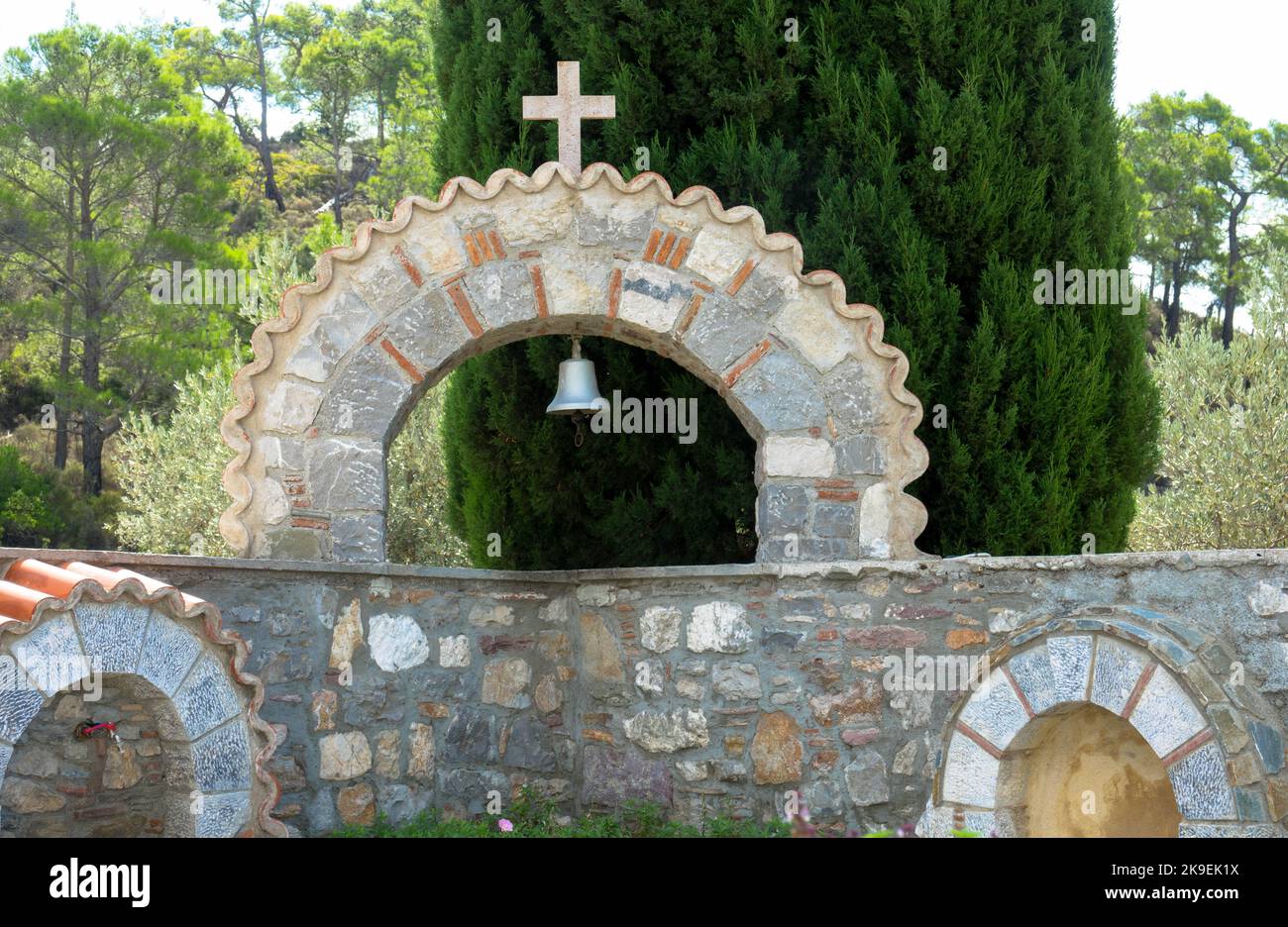 Sandsteinbogen mit Glocke und religiösem Kreuz vor einer wilden und romantischen Landschaft. Moni Thari Kloster, Rhodos Insel, Griechenland. Stockfoto