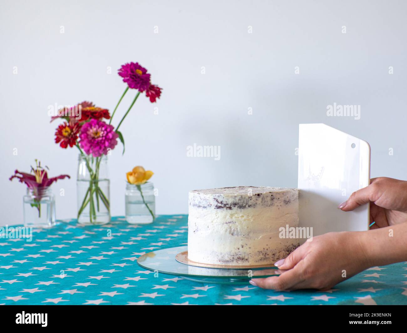 Die Creme mit einem Teigschaber von den Händen abgleichen und den runden Kuchen bedecken Stockfoto