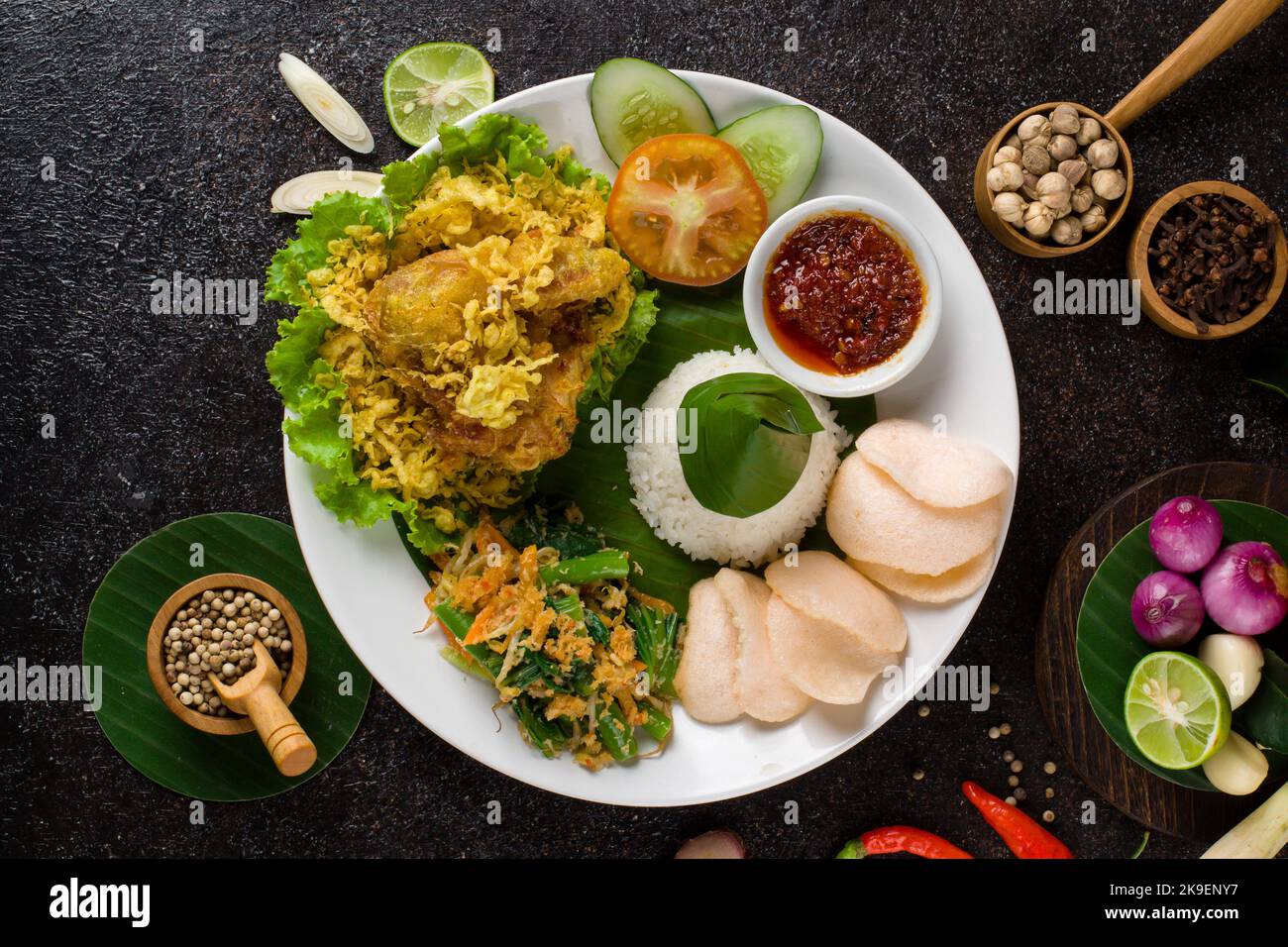 Ayam Goreng Lengkuas oder Gewürze gebratenes Huhn ist ein traditionelles indonesisches gebratenes Huhn mit frischen Kräutern, Gemüse und Chilisauce, serviert in weißen pl Stockfoto