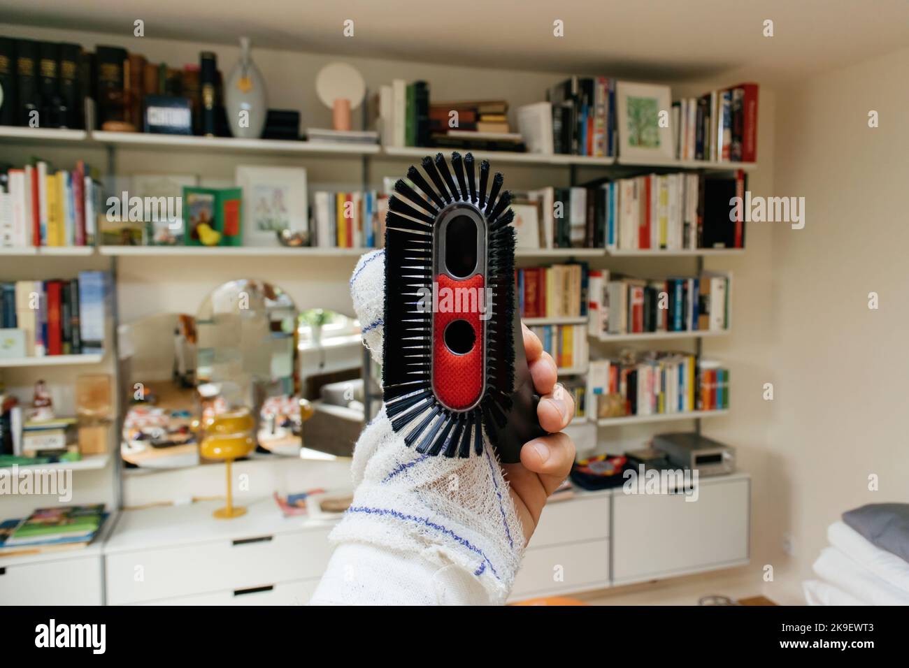Männliche Hand mit einer bandagierten Hand, die die Vakuumbürste hält - mehrere Regale im Wohnzimmer Stockfoto
