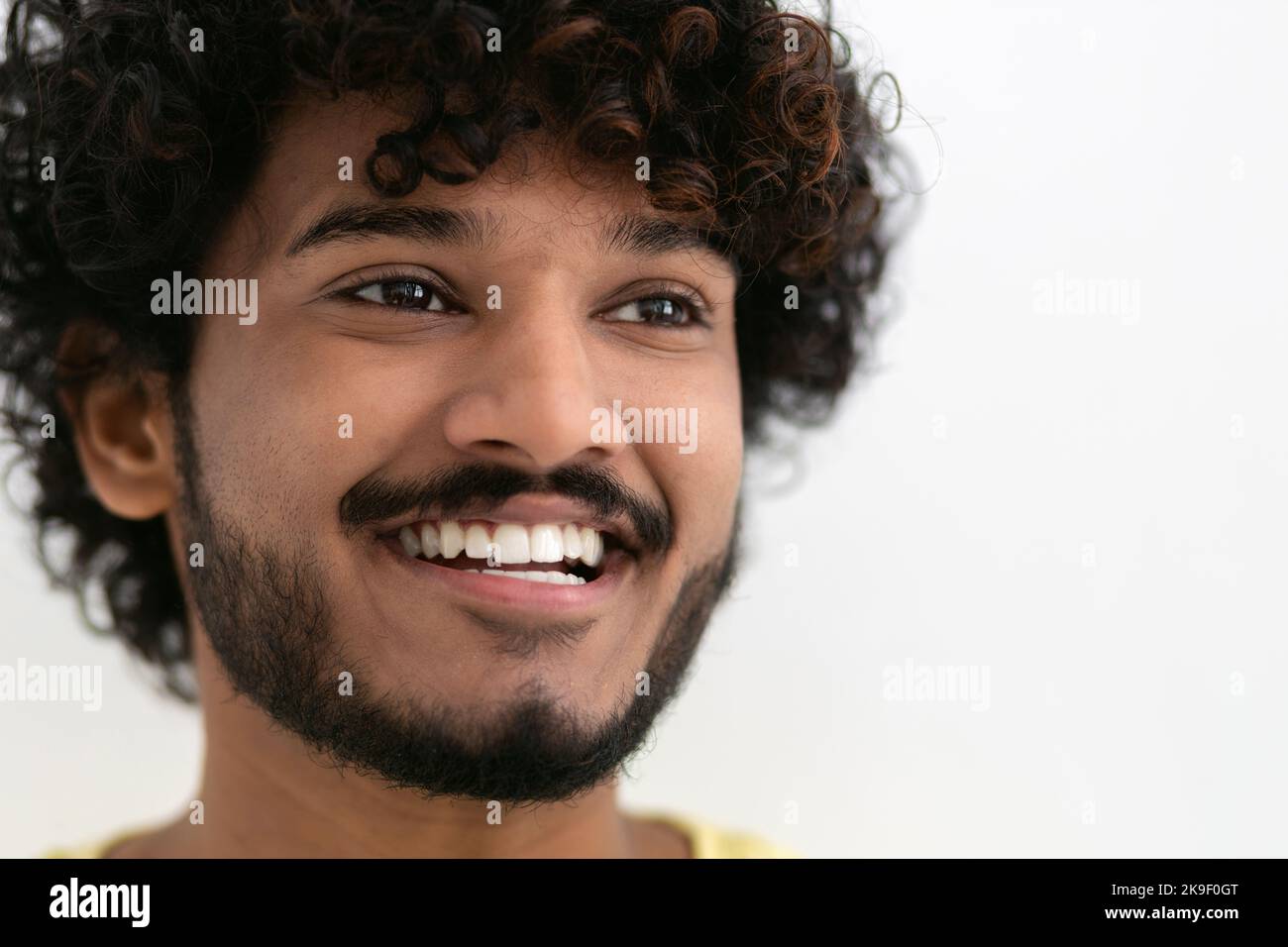 Portrait junger glücklicher, positiver Inder mit weißen Zähnen und lockigen Haaren, die auf weißem Hintergrund breit lächeln Stockfoto