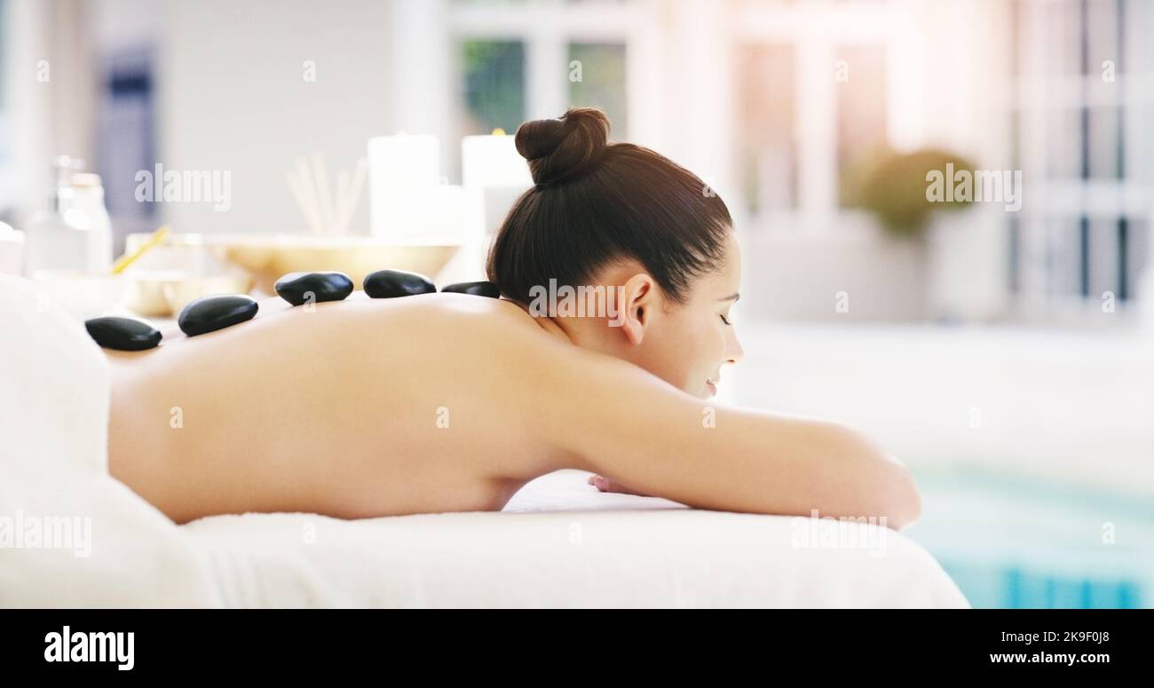 Unsere Behandlungen werden Sie garantiert verjüngen. Eine junge Frau bekommt eine Hot Stone Massage in einem Spa. Stockfoto