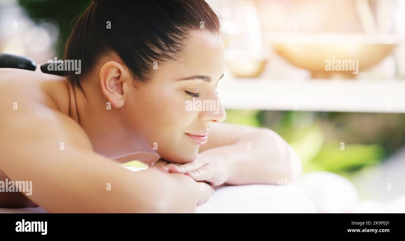 Eine junge Frau, die eine Hot Stone Massage in einem Spa bekommt, ist hier genau richtig. Stockfoto