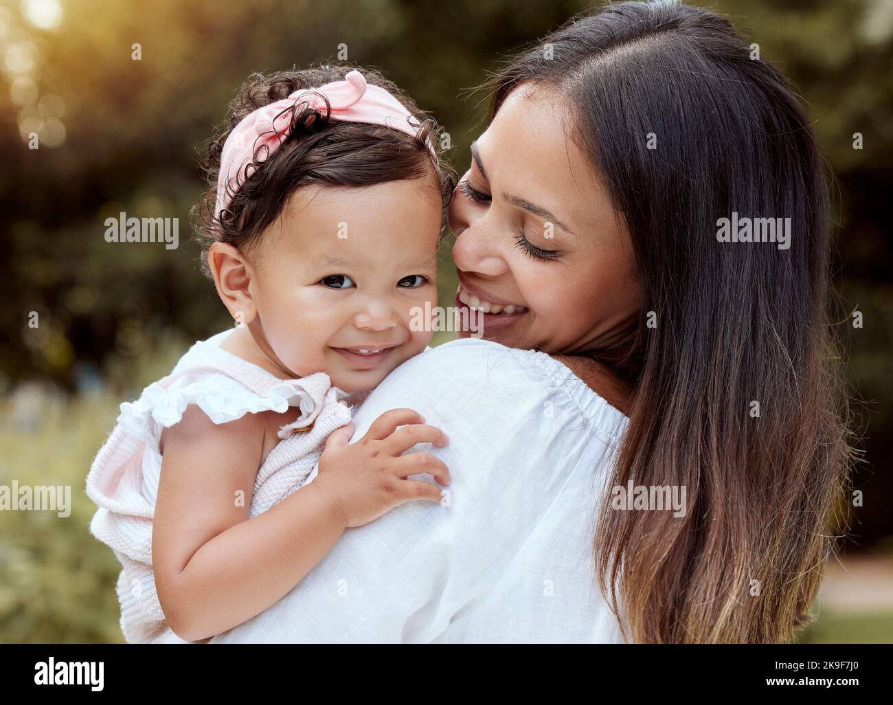 Glückliche Mutter mit Mädchen Baby Umarmung in einem Park mit Sommerliebe, Lächeln und Pflege oder Wachstum Entwicklung Wellness. Glücklich latino Mutter mit Kind im Porträt Stockfoto