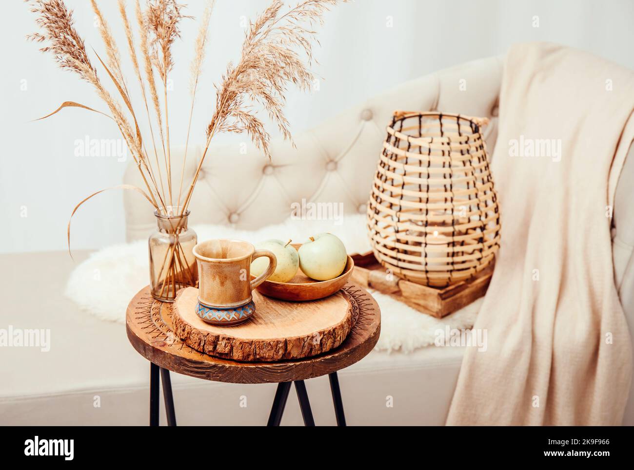 Cozycore oder cottagecore Konzept, warm weich braun beige Interior Design-Objekte. Kuscheliges Wollkaro auf dem Sofa, Kerzenbrenner in Holzlaterne, Teetasse. Stockfoto