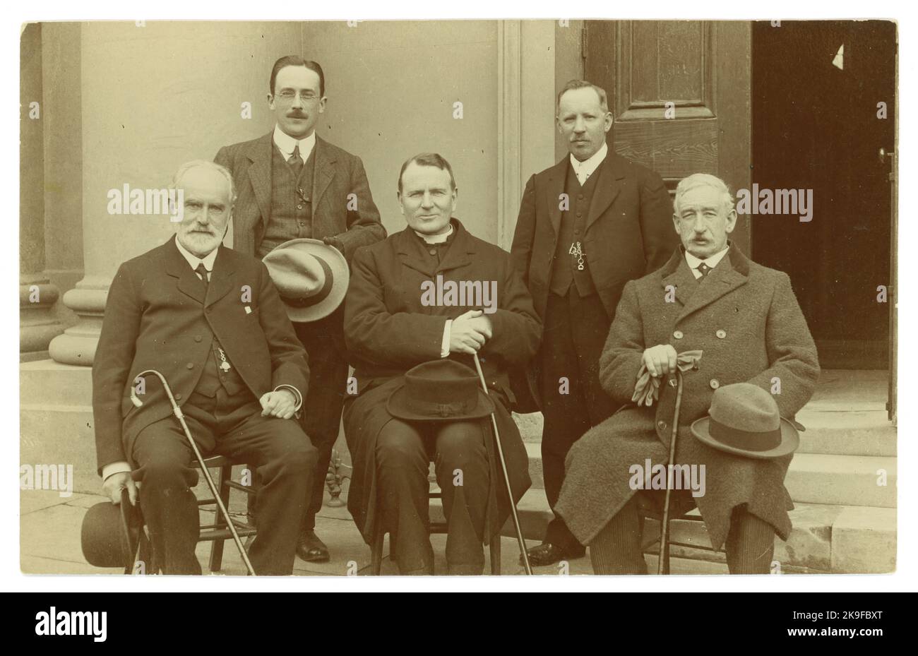 Originalpostkarte aus dem frühen 20. Jahrhundert mit wohlhabenden Herren, die Homburger Hüte, Spazierstöcke, Anzüge mit Uhrenketten und Mänteln mit einem Geistlichen halten. Zwei der Männer haben Medaillen in Form eines Kreuzes. Die Männer sind vielleicht Säulen der lokalen Wirtschaft, etwa 1913-1919, Großbritannien Stockfoto