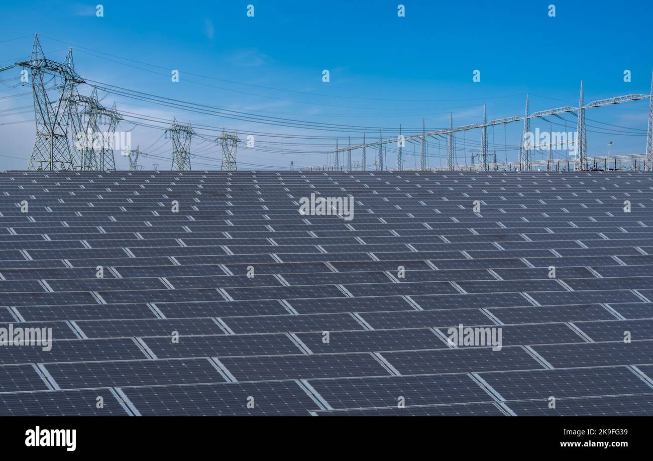 Sonnenkollektoren mit Hochspannungsmasten am blauen Himmel, Strom-Photovoltaik-Produktionsanlage mit großer Oberfläche von Photovoltaik-Modulen Stockfoto