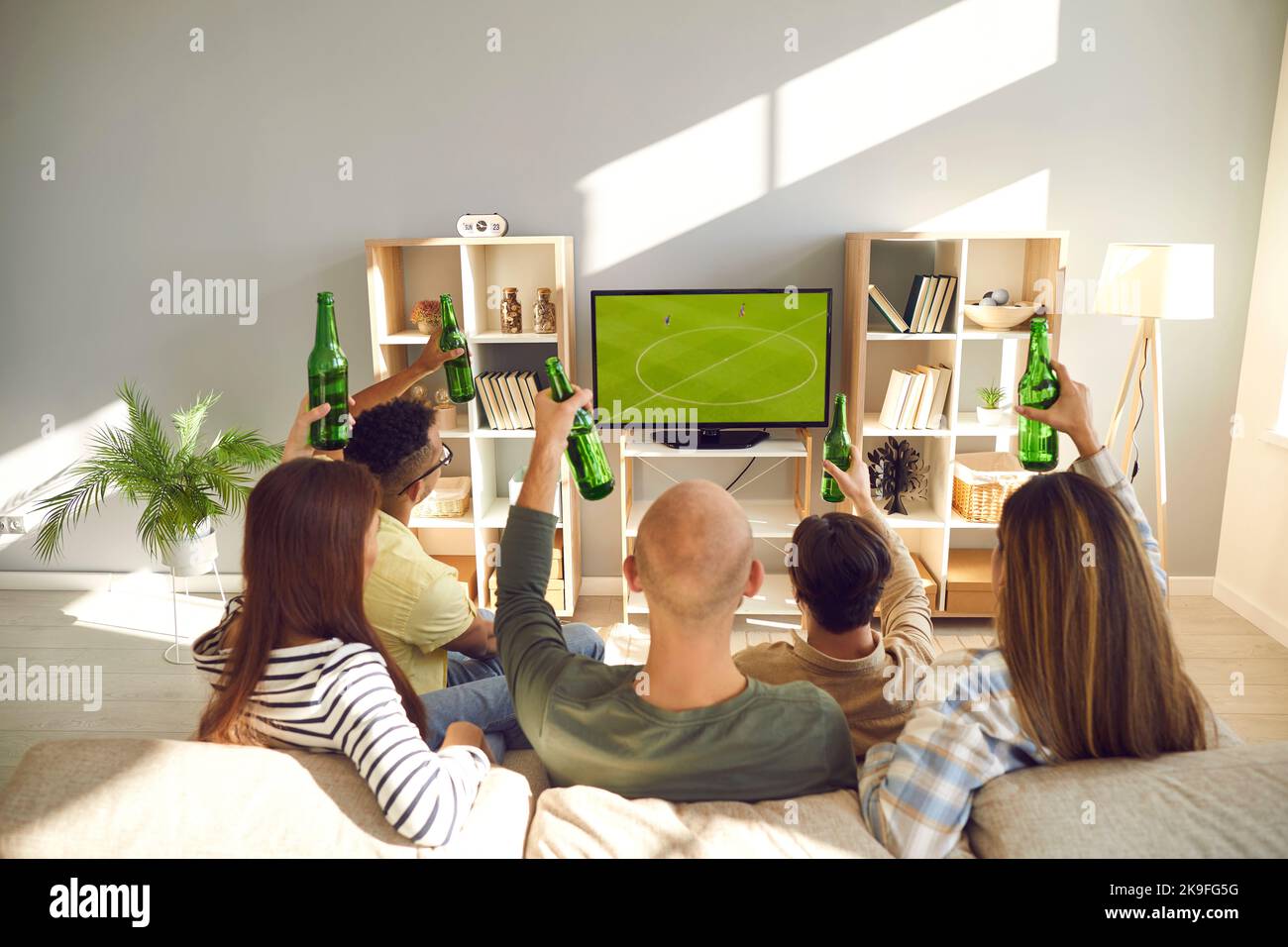 Eine Gruppe junger Freunde sitzt auf dem Sofa, schaut Fußball im Fernsehen und trinkt Bier Stockfoto