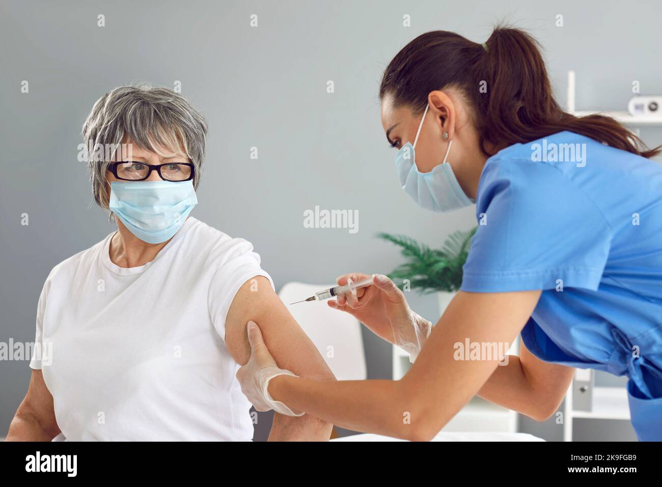 Ältere Frau in medizinischer Gesichtsmaske, die während des Infektionsausbruchs in der Klinik geimpft wird Stockfoto