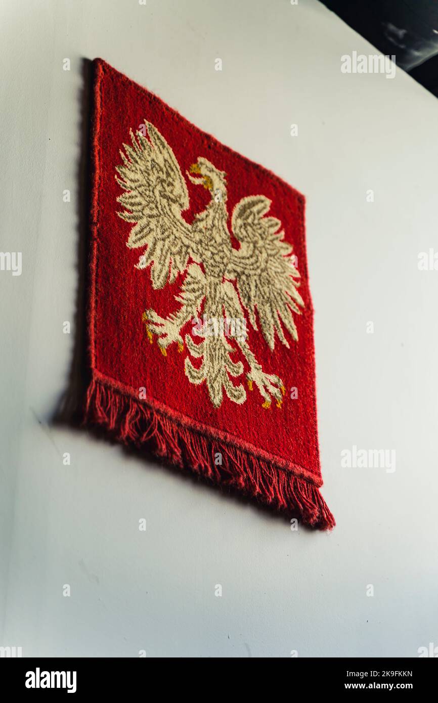 Vertikale Aufnahme des roten polnischen PRL-Emblems des weißen Adlers ohne Krone, die an der weiß-grauen Wand hängt. Altes Symbol Polens. Der Bube des Präsidenten der Republik Polen. Hochwertige Fotos Stockfoto
