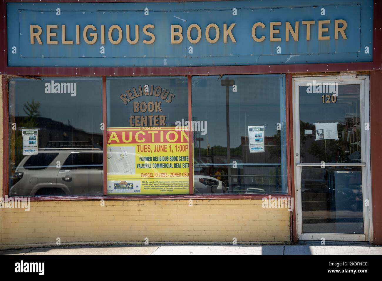 StoreFront einer religiösen Buchhandlung, die zur Versteigerung gestellt wurde, mit einem Spiegelbild eines weißen Autos in den Fenstern Stockfoto