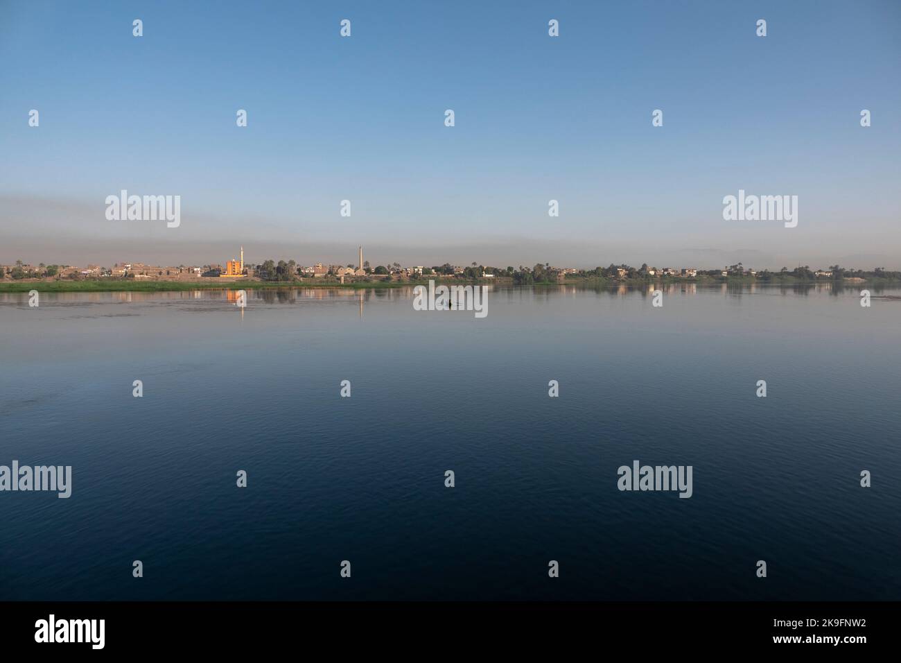 Sehr entferntes Panorama des Nil-Ufers mit einigen Häusern mit großer Wasserfläche im Vordergrund und einem kleinen Fischerboot in der Nähe des Ufers Stockfoto