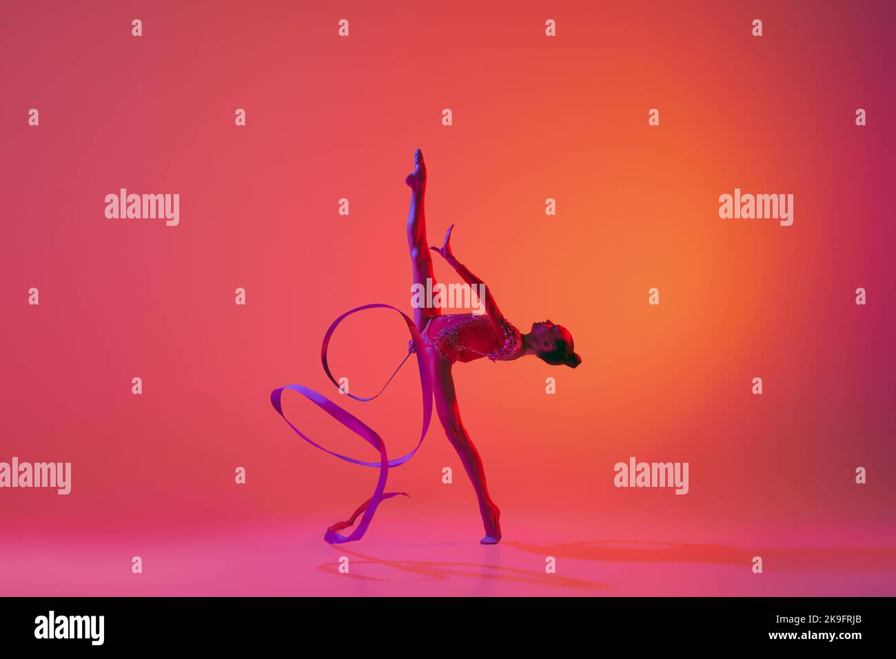 Junge flexible teen Mädchen rhythmische Turnerin in Bewegung, Aktion isoliert über rosa Hintergrund in Neonlicht. Sport, Schönheit, Wettkampf, Flexibilität Stockfoto