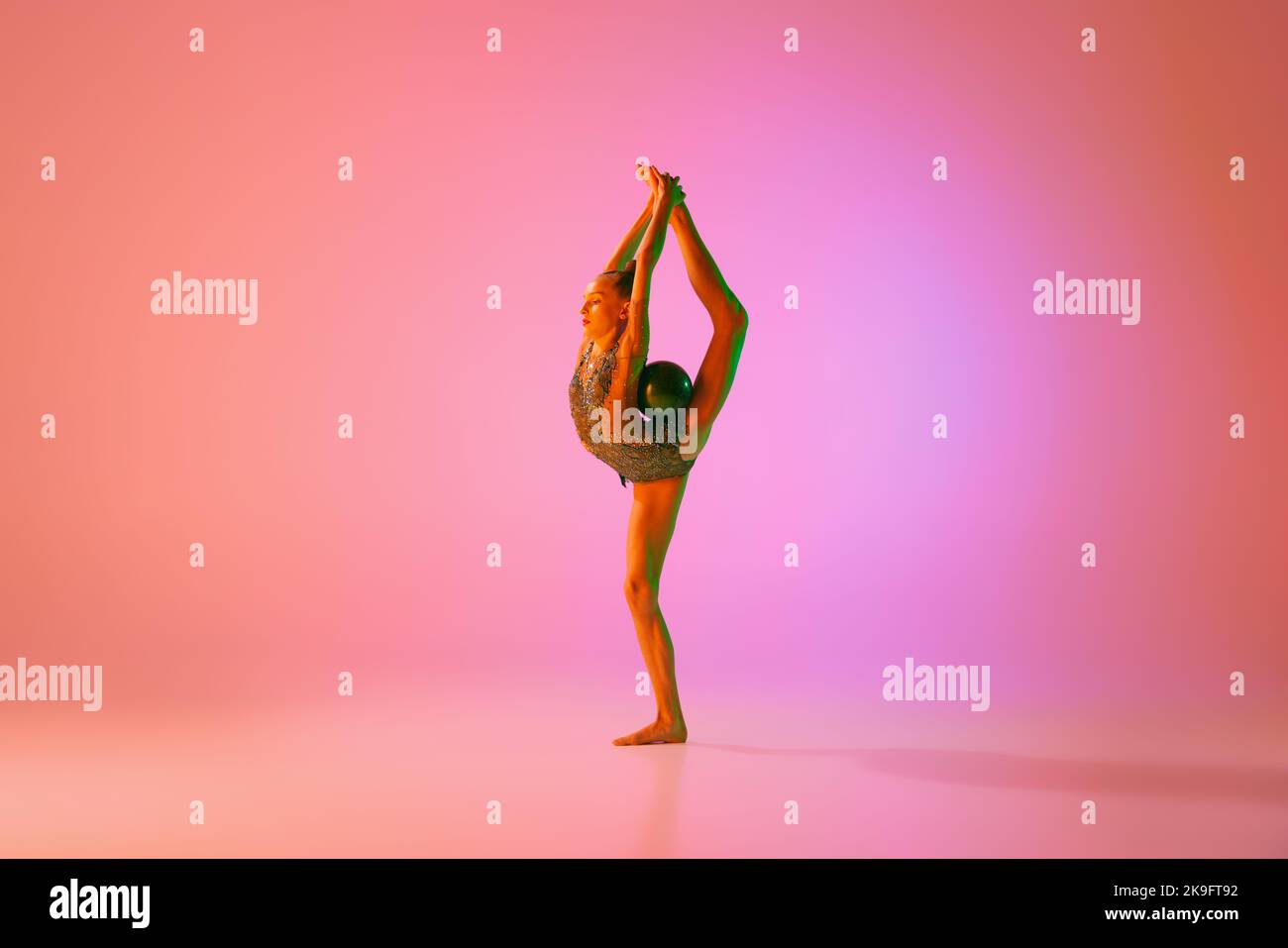 Junge flexible teen Mädchen rhythmische Turnerin in Bewegung, Aktion isoliert über rosa Hintergrund in Neonlicht. Sport, Schönheit, Wettkampf, Flexibilität Stockfoto