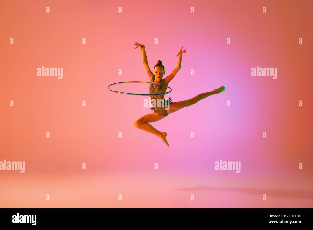 Junge flexible teen Mädchen rhythmische Turnerin springen isoliert über rosa Hintergrund in Neonlicht. Sport, Schönheit, Wettkampf, Flexibilität, aktiv Stockfoto