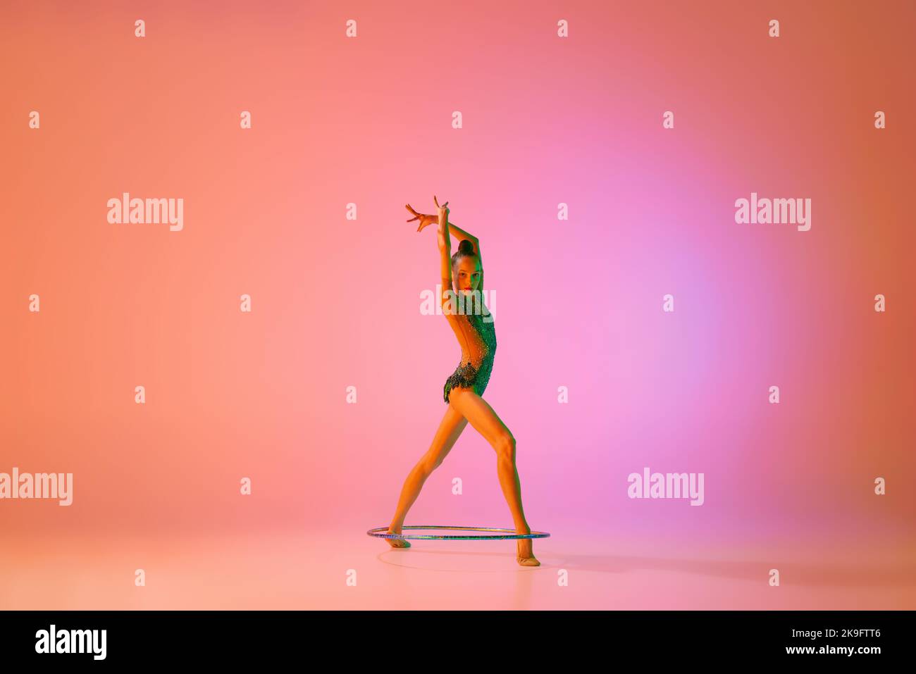 Anmut. Junge flexible teen Mädchen rhythmische Turnerin in Bewegung, Aktion isoliert über rosa Hintergrund in Neonlicht. Sport, Schönheit, Wettbewerb Stockfoto
