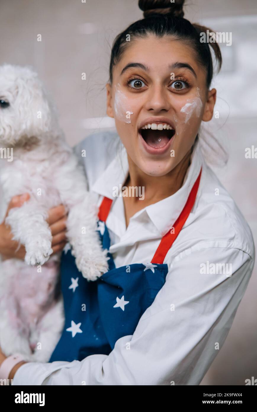 Lächelnde Frau in der Küche mit niedlichem weißen maltesischen Hund Stockfoto