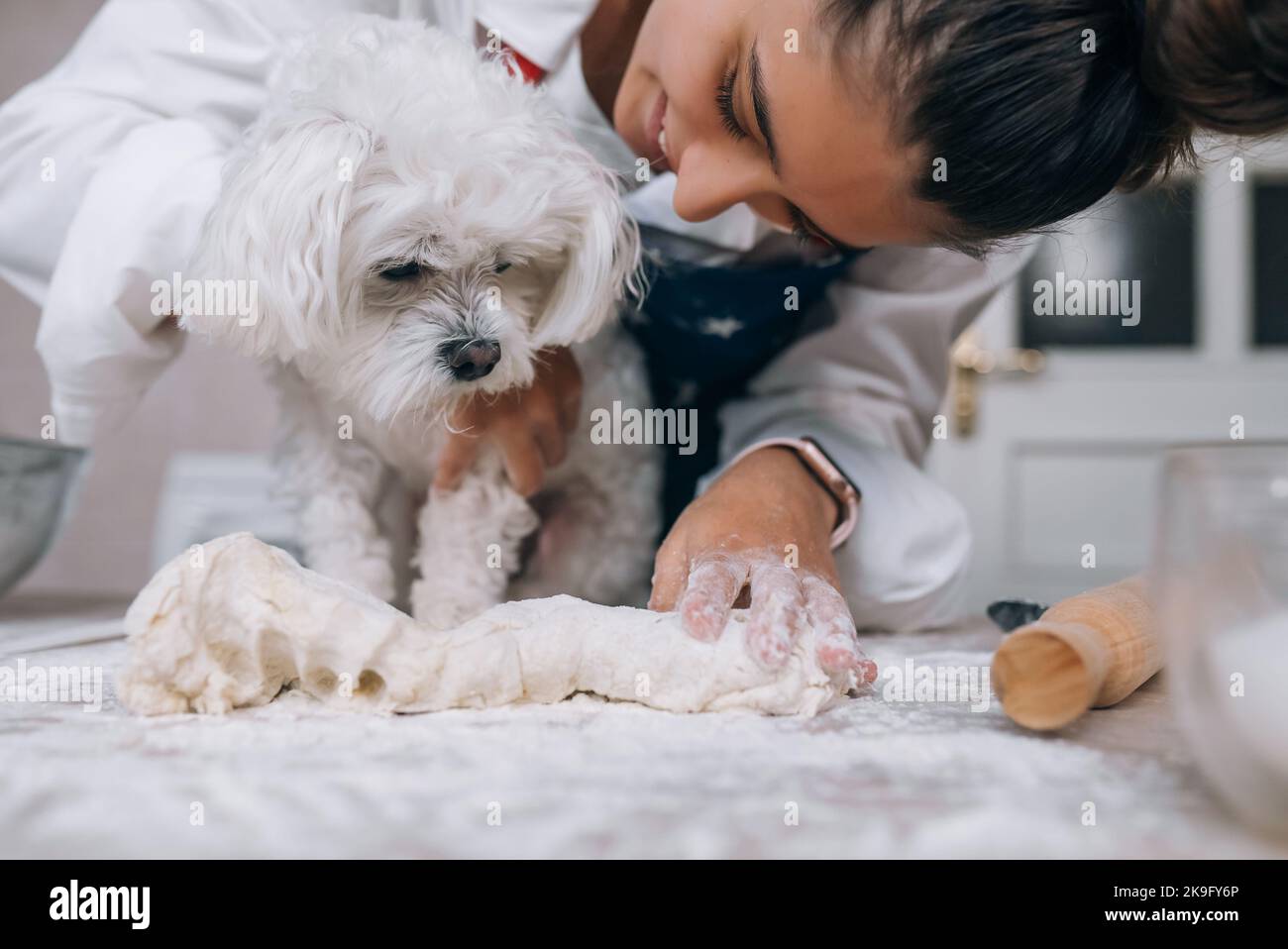 Frau in der Küche knetet den Teig mit ihrem Hund Stockfoto