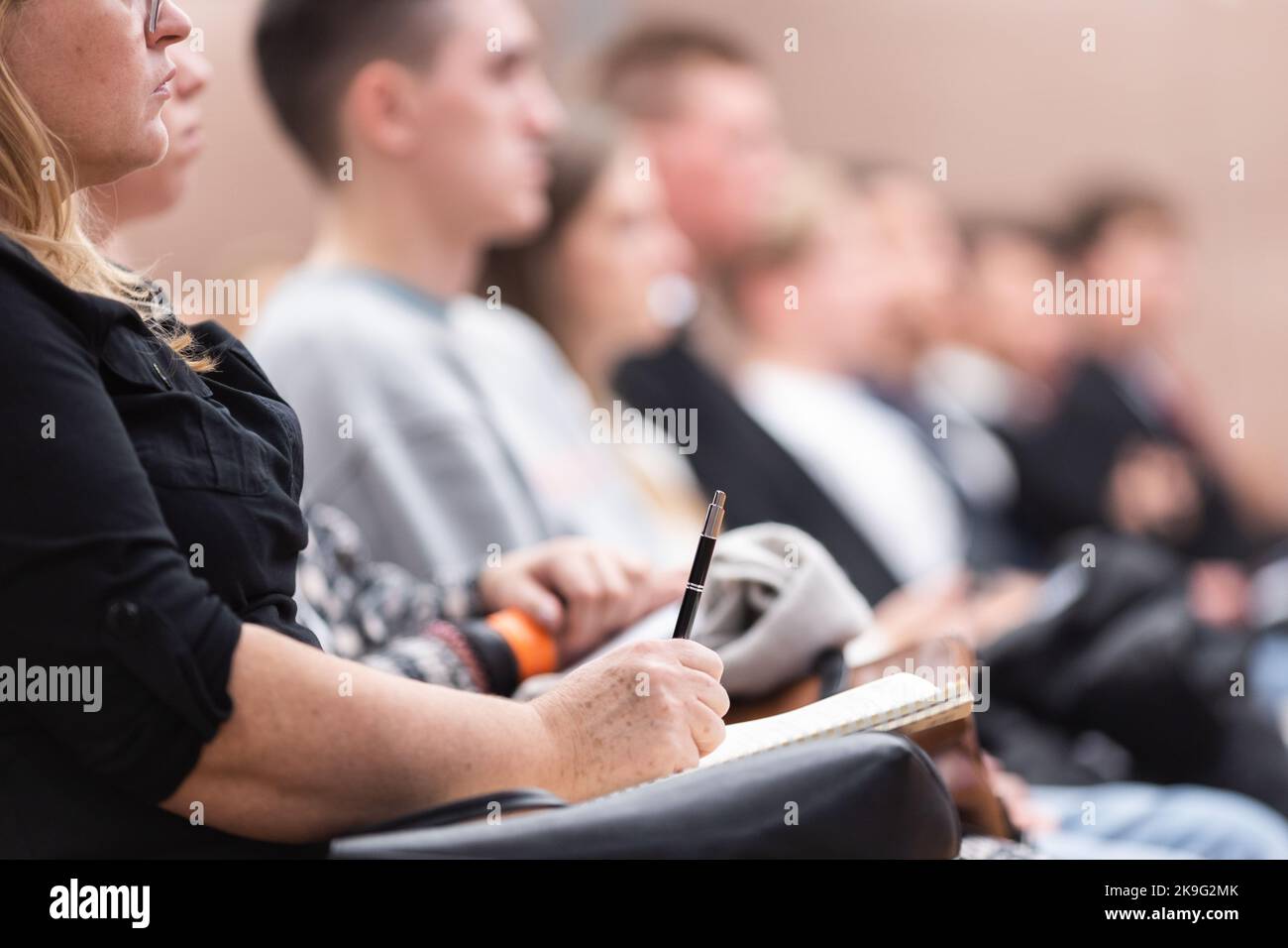 Weibliche Hände halten Stift und Notizbuch und machen Notizen bei der Konferenz Vortrag. Veranstaltungsteilnehmer im Konferenzsaal. Stockfoto
