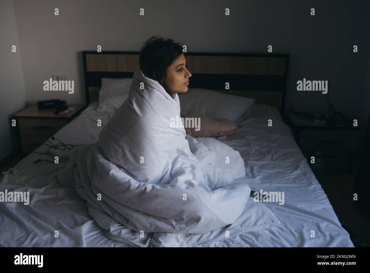 Eine junge Frau, die in eine Decke gehüllt und in die Ferne starrt Stockfoto