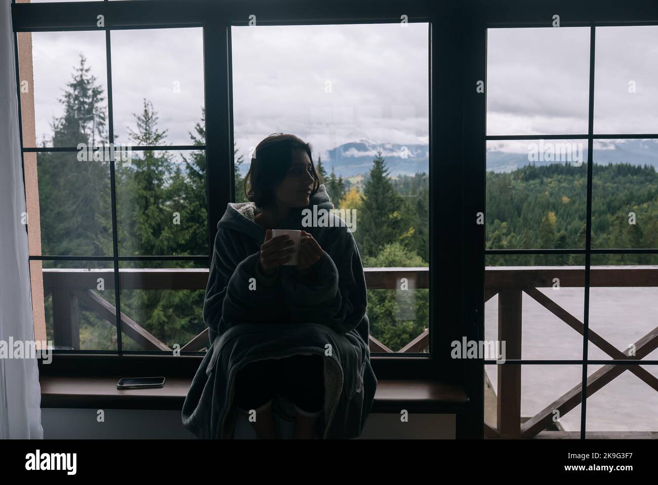 Silhouette einer Frau, die mit einem Becher auf der Fensterbank sitzt Stockfoto