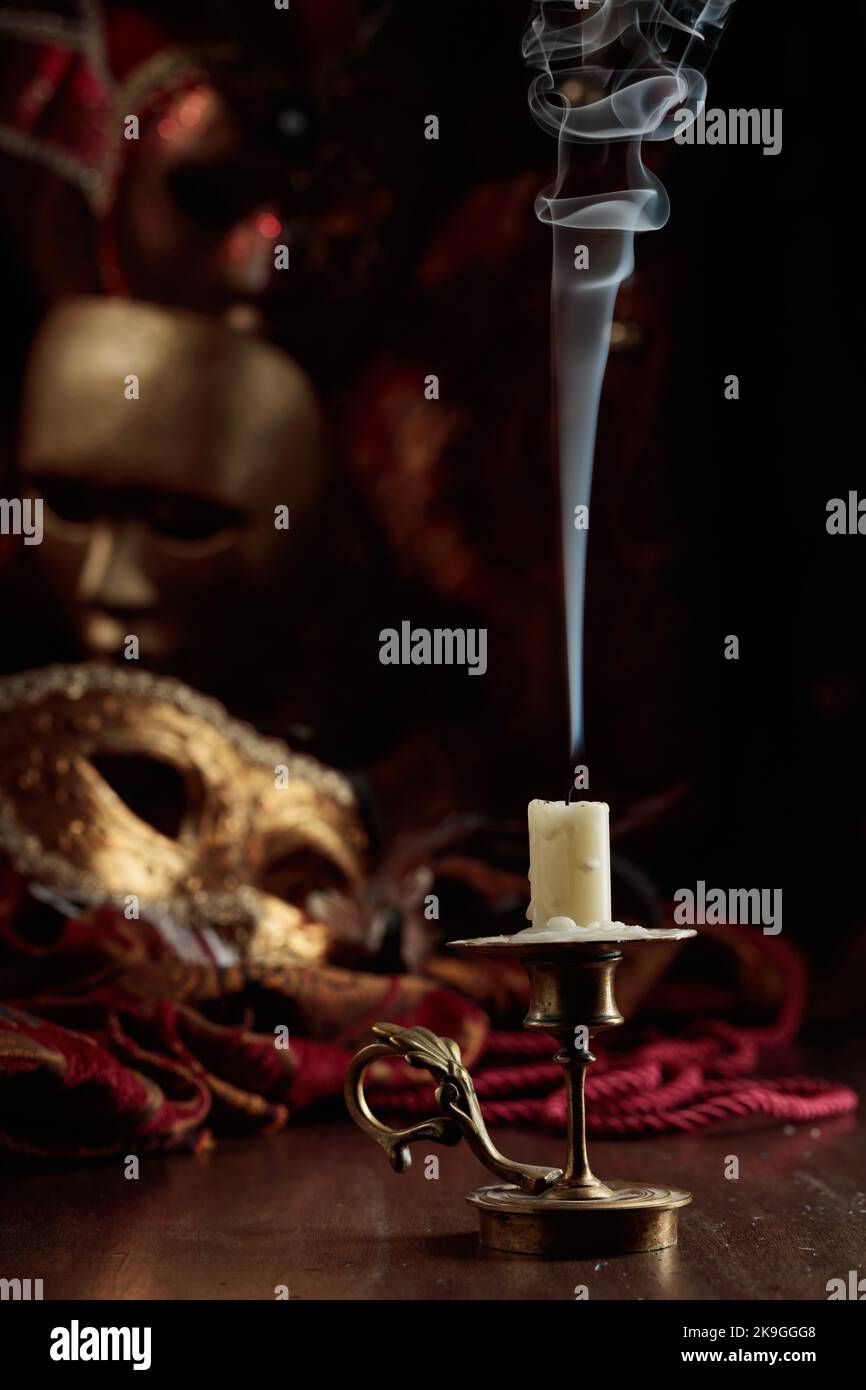 Stillleben mit einer erloschenen Kerze in einem alten Messingleuchter und Karnevalsmasken. Stockfoto