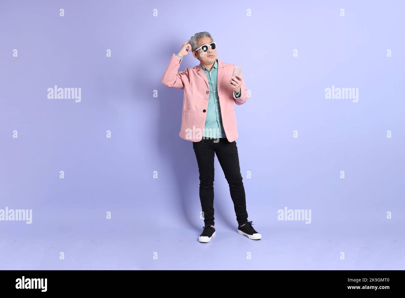 Der 40s-jährige asiatische Mann, der auf dem violetten Hintergrund mit eleganter Freizeitkleidung unterwegs ist. Stockfoto