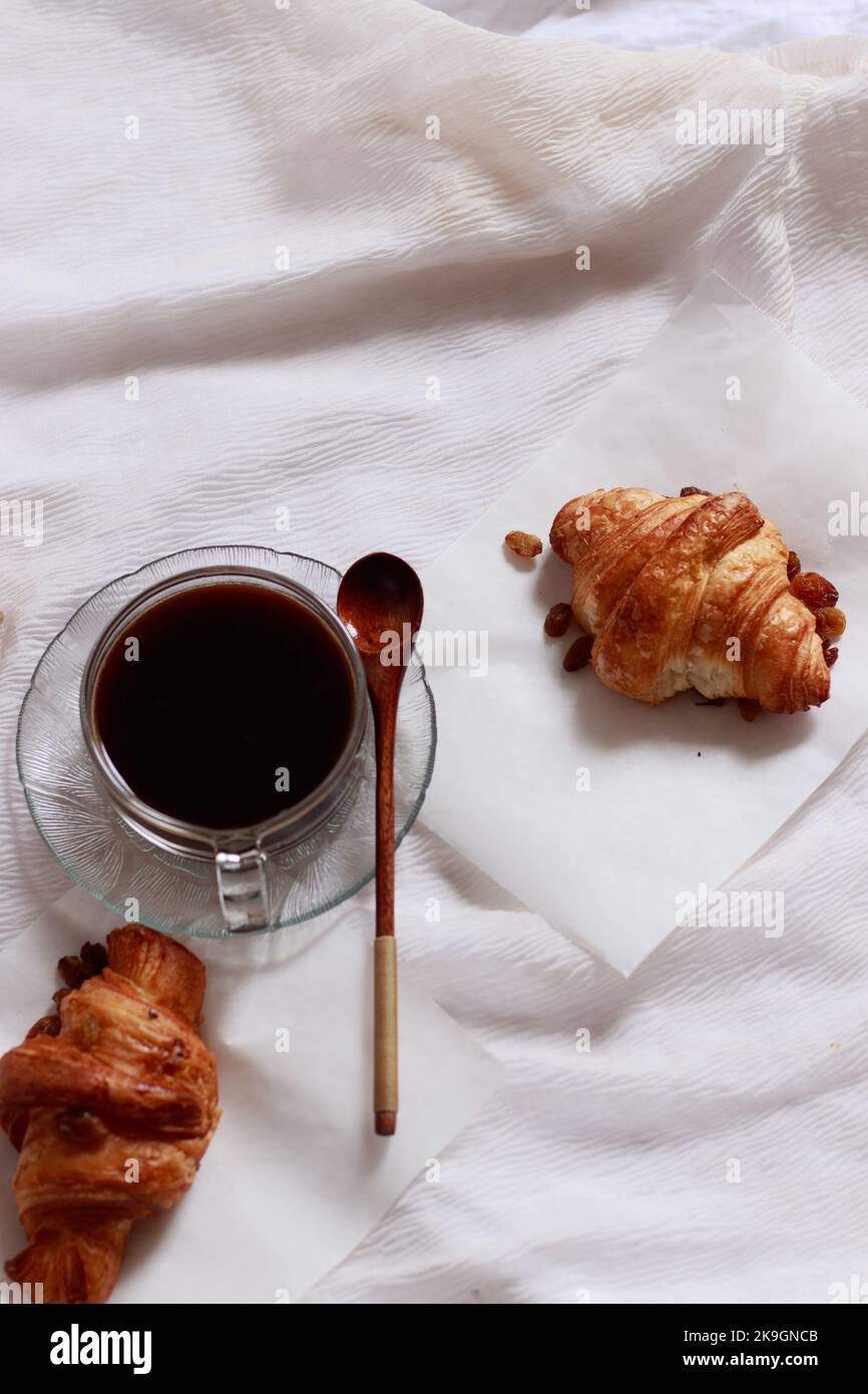Vertikale Aufnahme von frisch gebackenen Croissants und schwarzem Kaffee für ein einfaches französisches Frühstück Stockfoto