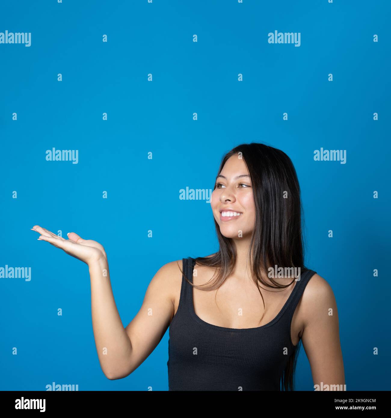 Junge trendige Frau mit großem Lächeln hält und präsentiert Kopierraum auf ihrer Handfläche isoliert auf blauem Hintergrund Stockfoto