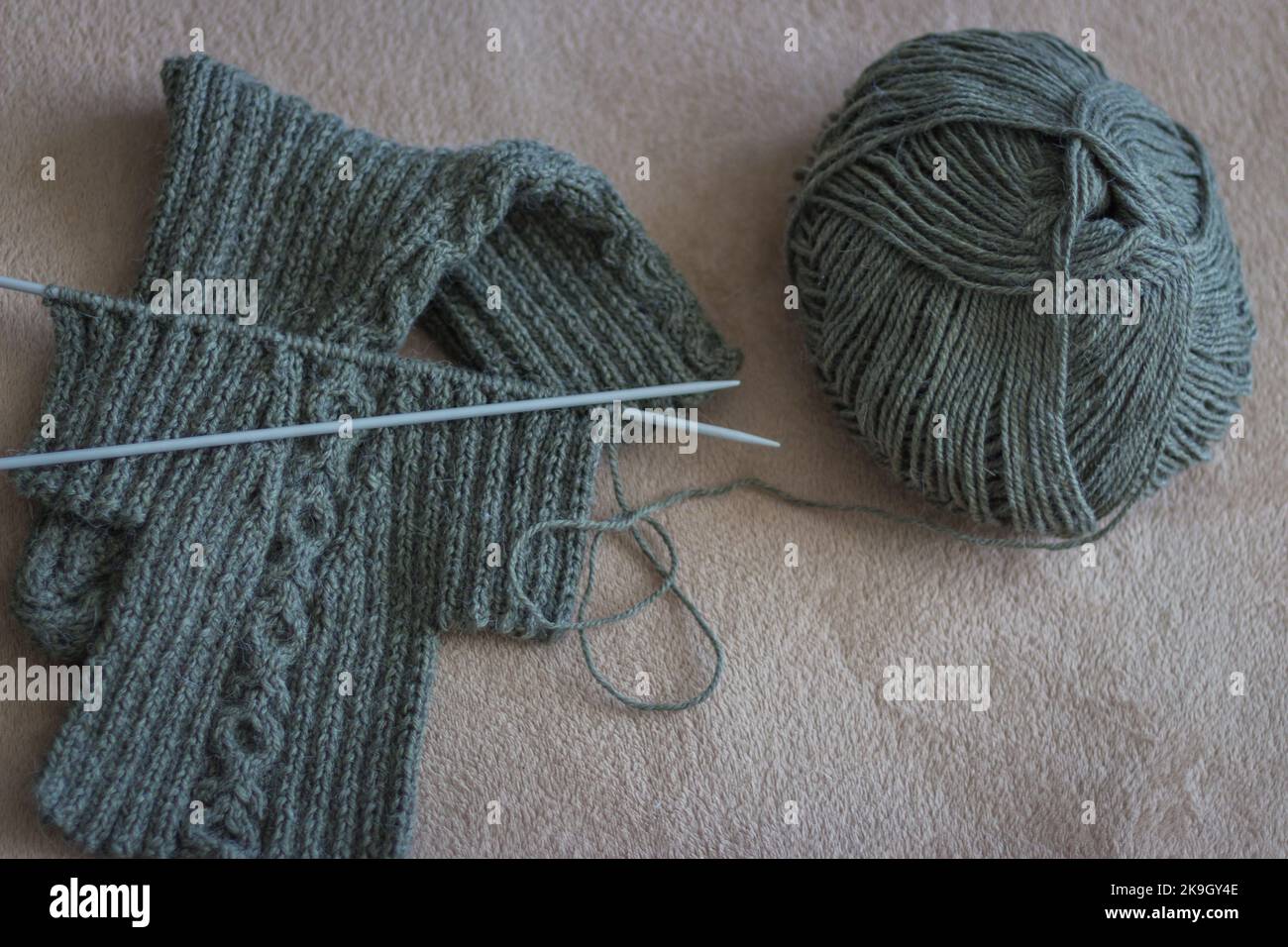 Grünes Strickgarn und Stricknadeln. Strickmode. Socken und Nadeln aus Wolle. Herbsthobby. Handwerkliche Kleidung. Winterhobby. Nadelarbeitskonzept Stockfoto