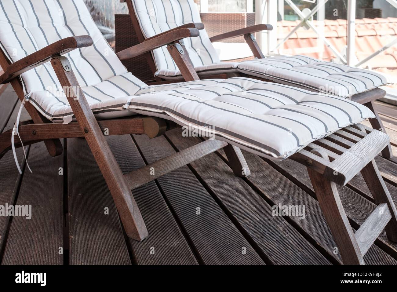 Leerer Holzdeckstuhl mit einem weichen Kissen auf der Terrasse, vor dem Hintergrund der Dächer. Stockfoto