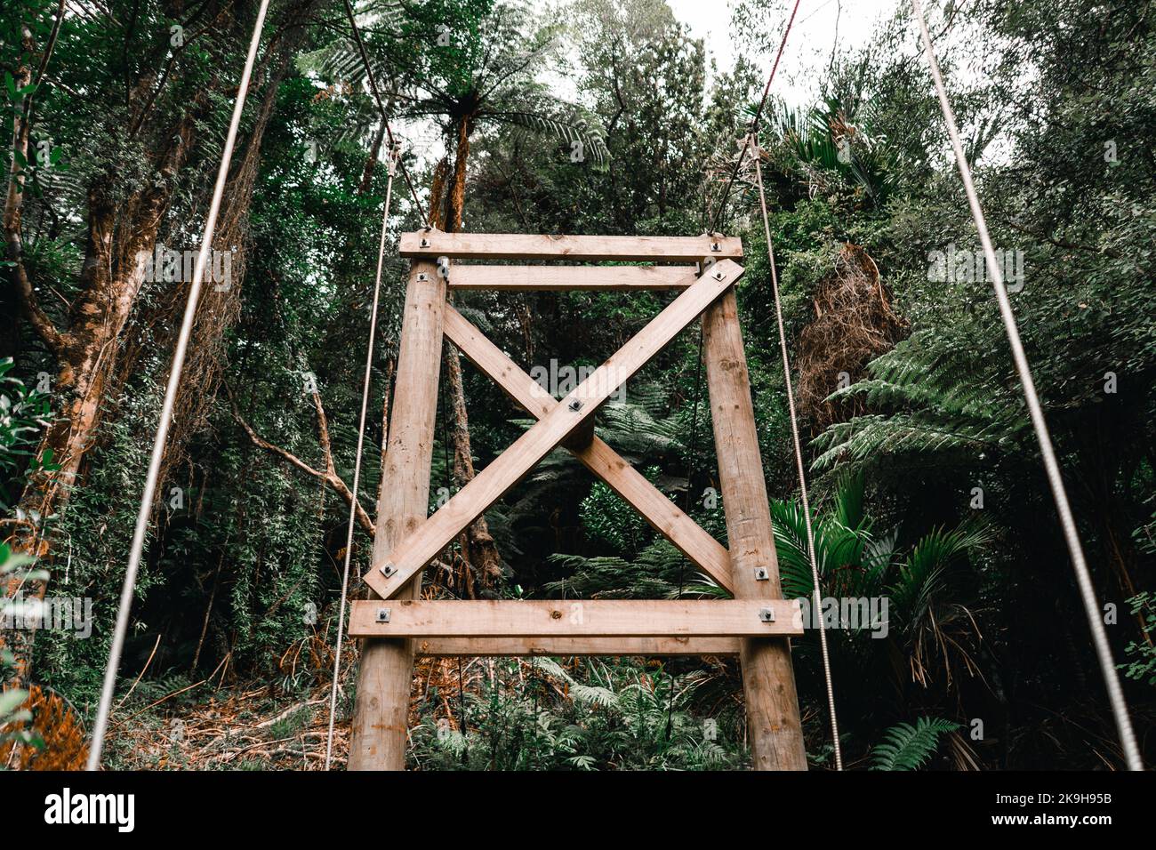 Holzsäulen und Schrauben, die die dicken Metalldrähte der Hängebrücke halten, die den Wald über dem Fluss in Donut Island durchquert, neu Stockfoto
