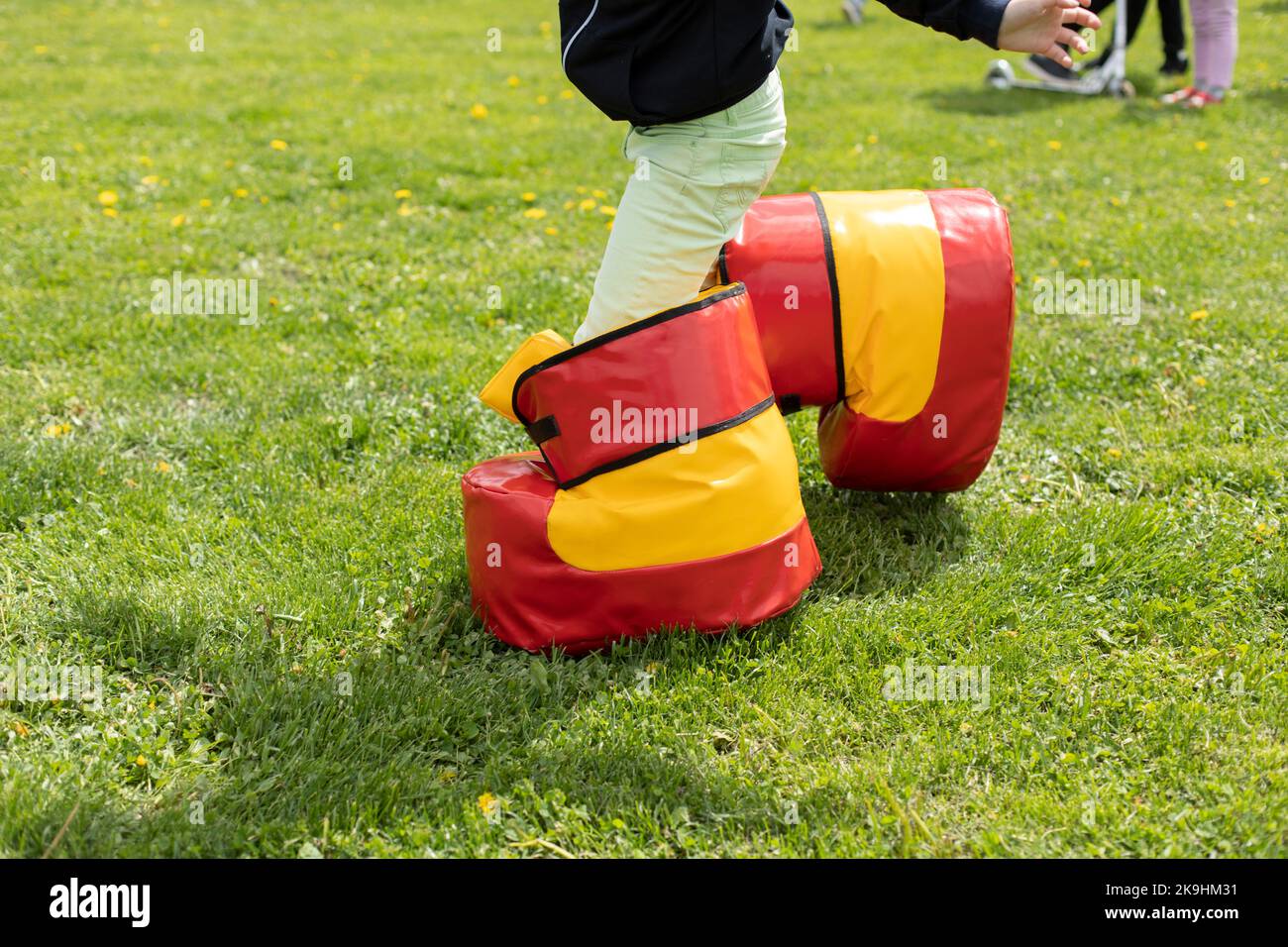 Lustige Schuhe für das Spiel. Spaß Urlaub des Kindes im Sommer. Unterhaltung auf grünem Gras. Spielen auf dem Rasen. Kind in unbequemen Schuhen. Stockfoto