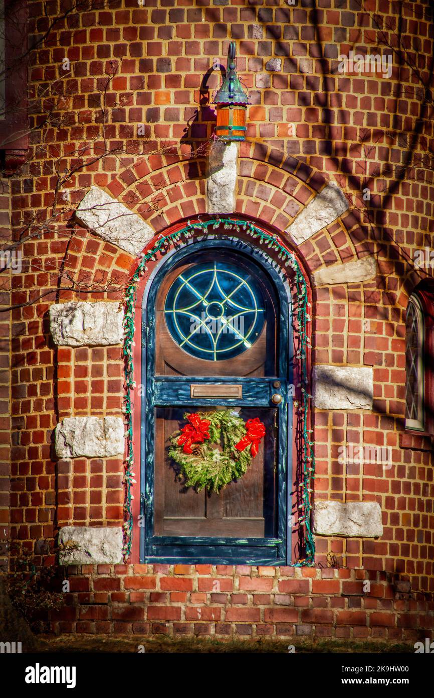 Gewölbte Tür im Turm aus Backstein Haus mit Weihnachtsbeleuchtung und runden Buntglasfenster und Urlaub Kranz Stockfoto