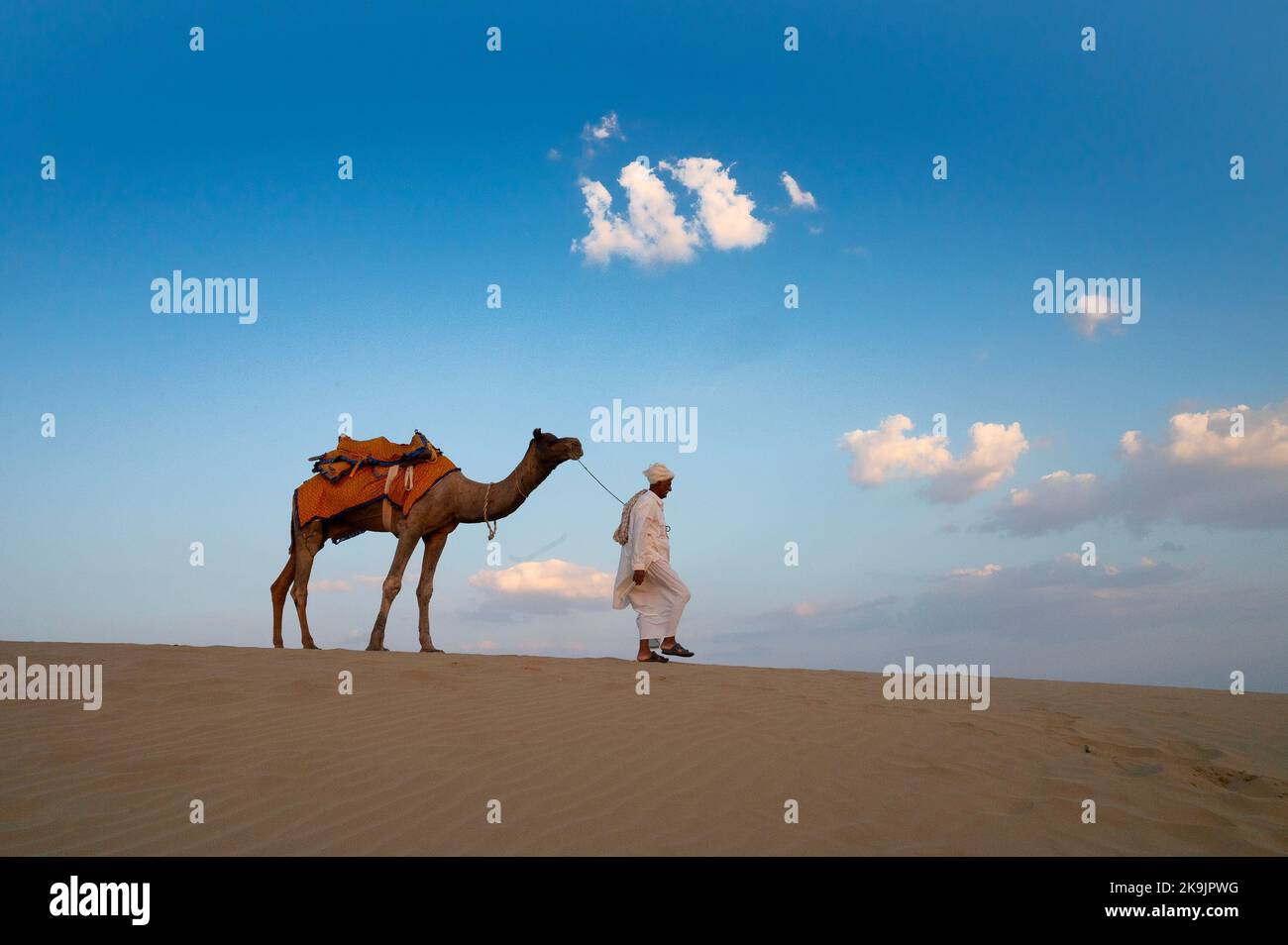 Thar-Wüste, Rajasthan, Indien - 15.. Oktober 2019 : Alter Kamelreiter, der sein Kamel, Camelus dromedarius, zurücknimmt, nachdem er in der Dämmerung in Sanddünen touristisch reitet. Stockfoto